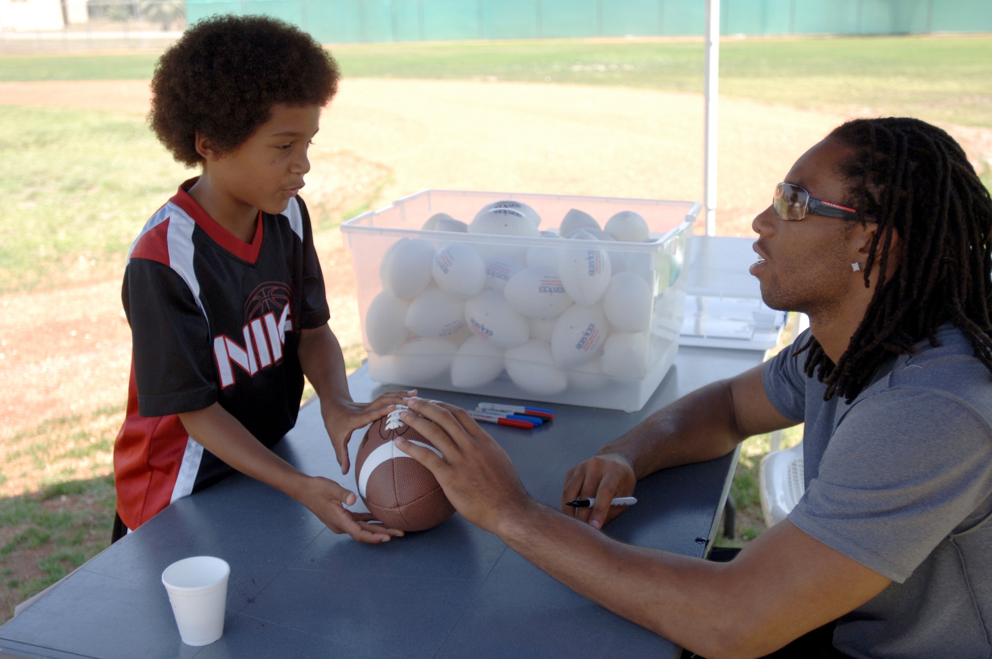 Eight-year-old DeShaun Moorer hands Arizona Cardinals wide receiver Larry Fitzgerald a football to sign during an autograph session at Incirlik Air Base, Turkey, on Wednesday, June 21. (U.S. Air Force photo/Senior Airman Larry Reid Jr.) 

