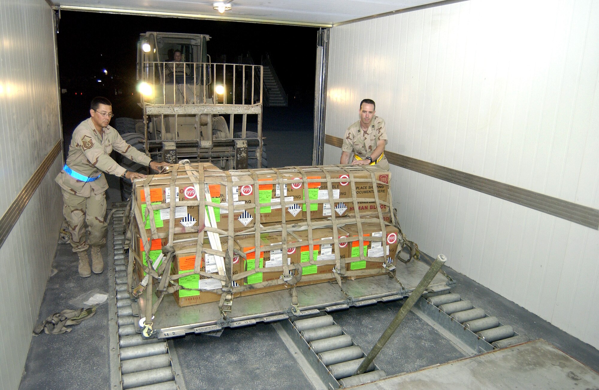 Airman 1st Class Rachel Castaneda maneuvers a forklift carrying a palletized blood and plasma shipment at the 379th Expeditionary Medical Group's Expeditionary Blood Transshipment System at a forward operating base in Southwest Asia. Master Sgt. Ed Juraszek and Capt. Scott Corey help guide the pallet into a refrigerated storage unit at the flightline where the blood stays until it is put on an aircraft going to forward operating bases. Airman Castaneda is assigned to the 379th EMG. (U.S. Air Force photo/Tech. Sgt. Chuck Marsh) 
