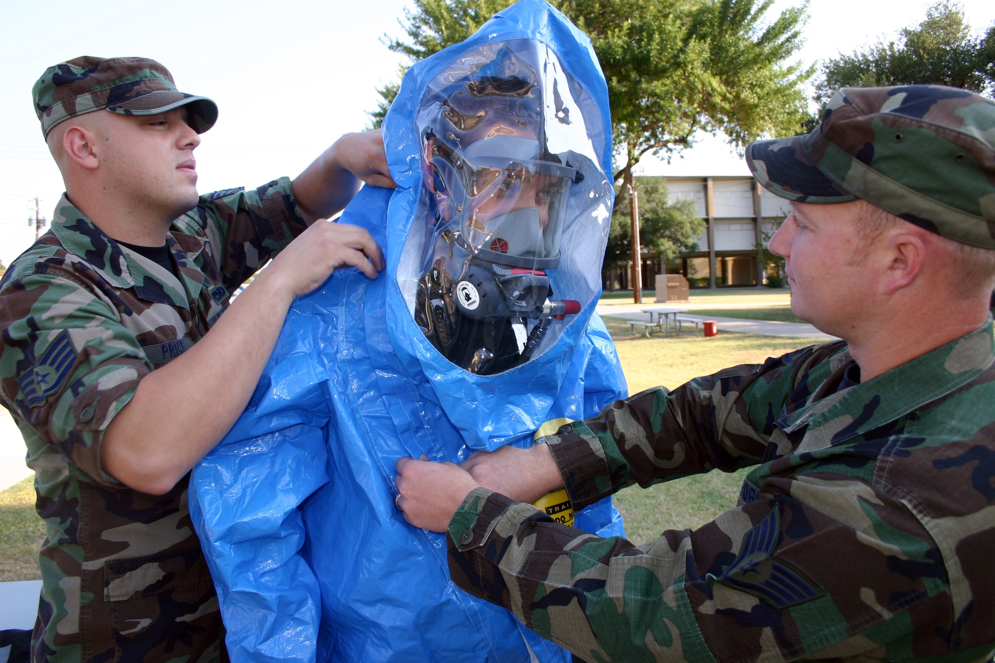 Staff Sgts. Christopher Price (left) and Chad Brock help Airman 1st Class Corey Hayes into a hazardous-material suit, so he can respond to a simulated toxic industrial spill at Lackland Air Force Base, Texas, on Wednesday, June 28. The suit is worn when responding to a possible chemical, biological, radiological, nuclear or high-yield explosive attack. The Airmen are bioenvironmental engineer apprentices with the 59th Medical Wing. (U.S. Air Force photo/Master Sgt. Kimberly Spencer)