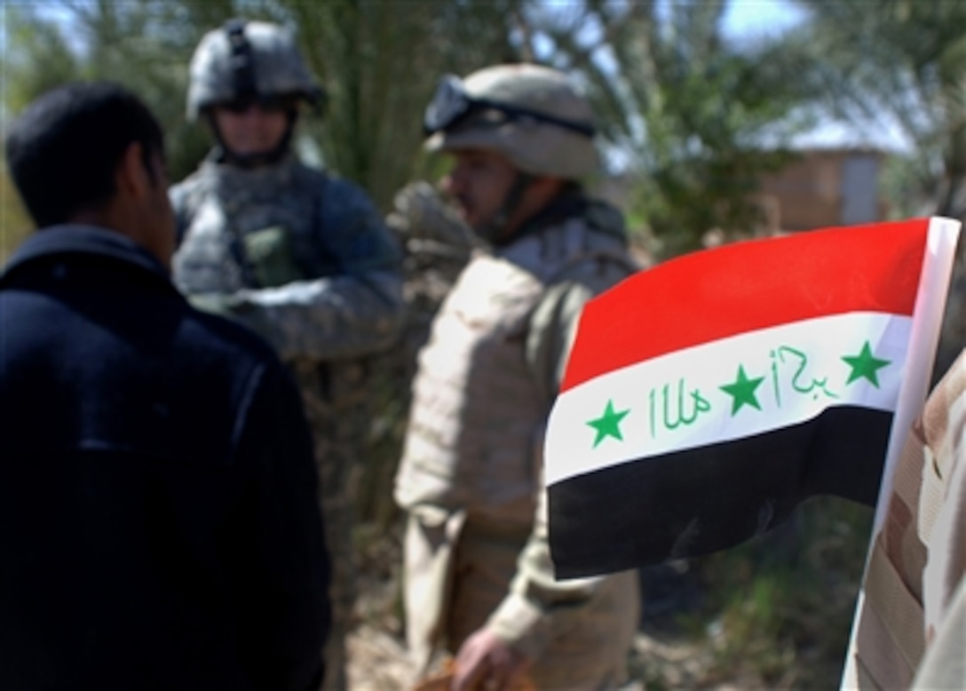 An Iraqi flag adorns an Iraqi soldier's uniform as a U.S. Army soldier and his interpreter talk with a local farmer during a mission to Taji, Iraq, March 11, 2006. 