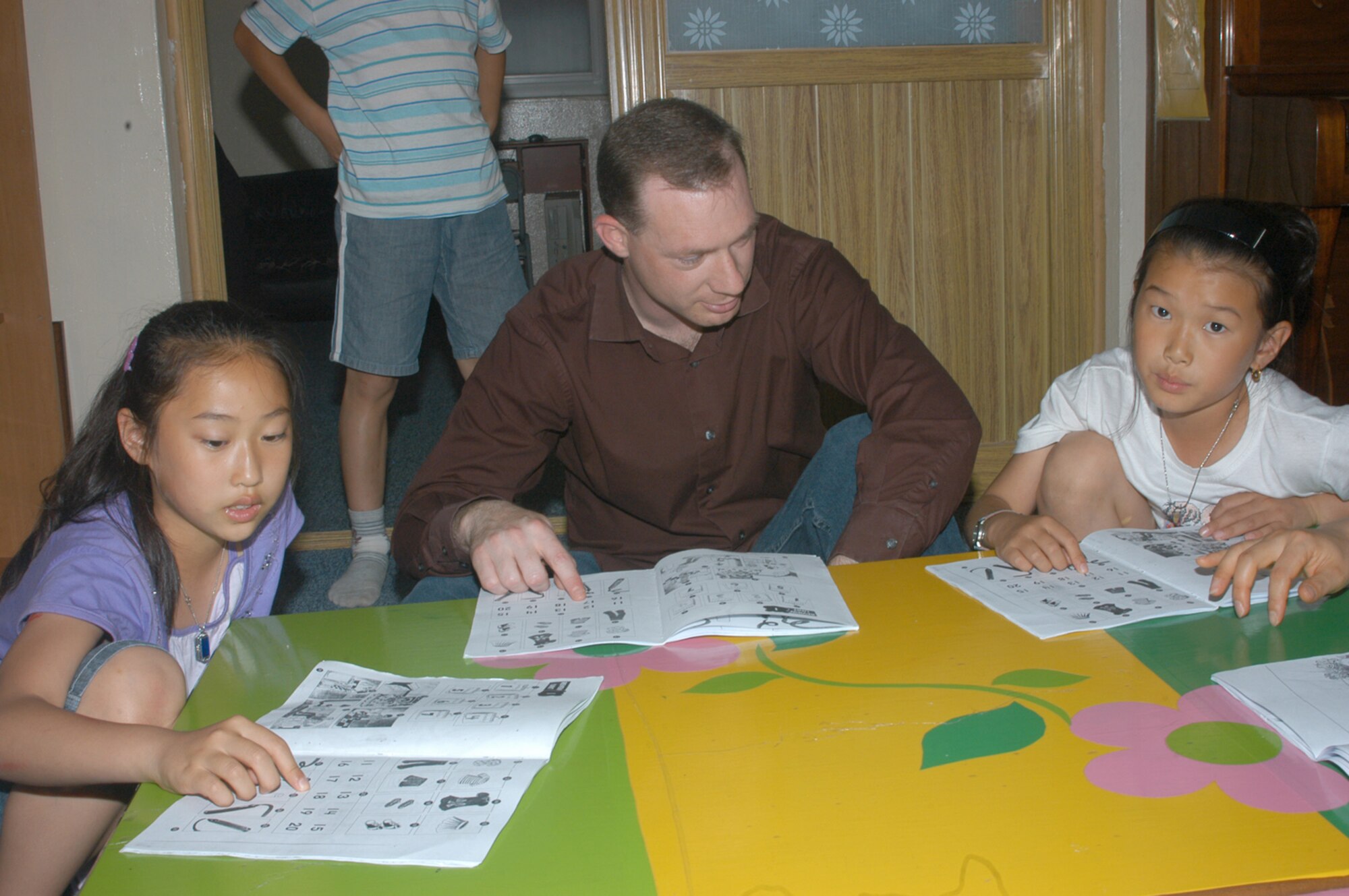 KUNSAN AIR BASE, Republic of Korea -- Tech. Sgt. Charles Campbell reads over an English picture book June 14 with a Korean student. Several members of the Air National Guard visited the Ilmagwon children's orphanage to help teach English. (Air Force photo by Staff. Sgt. Becky Nelson)                                
