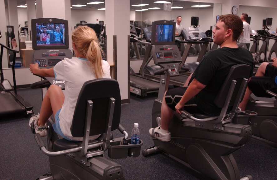MINOT AIR FORCE BASE, N.D. -- Heather Thompson and  Michael Patterson ride stationary bikes while watching TV at the McAdoo Sports and Fitness  Center June 28, 2006. Most of the center’s new cardio equipment comes with its own TV.  The newly renovated center cost more than $9.5 milion and took more than 18 months to complete. (photo by Airman 1st Class Joe Rivera)