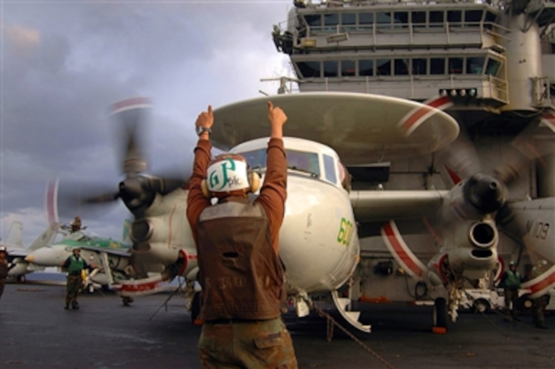 A U.S. Navy sailor, assigned plane captain duties with the “Liberty Bells” of Carrier Airborne Early Warning Squadron 115, signals to the pilot of an E-2C Hawkeye that pre-flight checks are complete prior to launching from the flight deck of the aircraft carrier USS Kitty Hawk in the South China Sea, Dec. 7, 2005. 