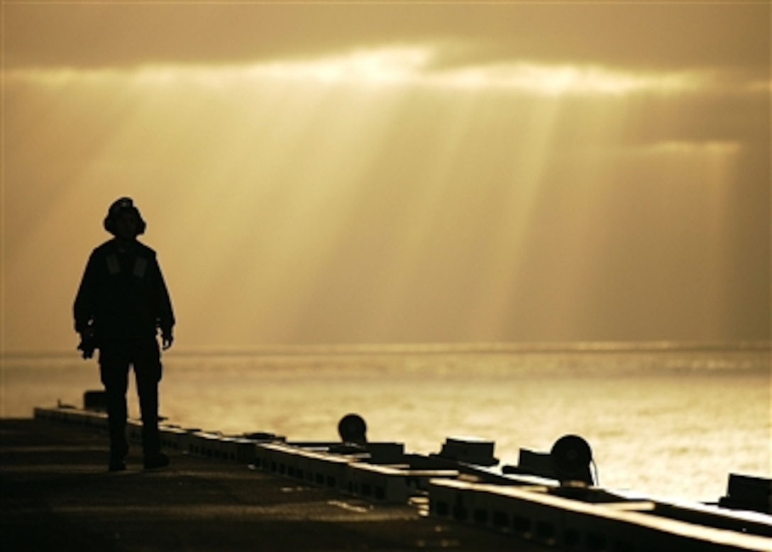 A sailor walks on the flight deck of the Nimitz-class aircraft carrier USS Abraham Lincoln as the sun rises over the bow, Sept. 19, 2005. Lincoln and embarked Carrier Air Wing 2 are currently conducting quarterly surge sustainment training off the coast of Southern California.