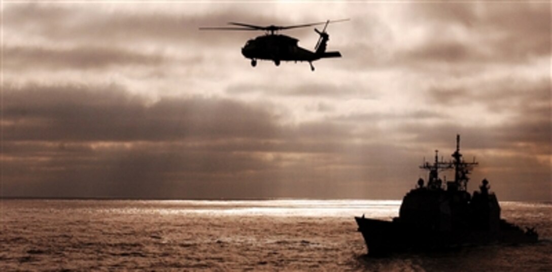 The guided missile cruiser USS Lake Champlain maneuvers off the coast of Southern California as an MH-60S Seahawk helicopter, assigned to the "Black Jacks" of Helicopter Sea Combat Squadron 21, flies overhead, Oct. 30, 2005.