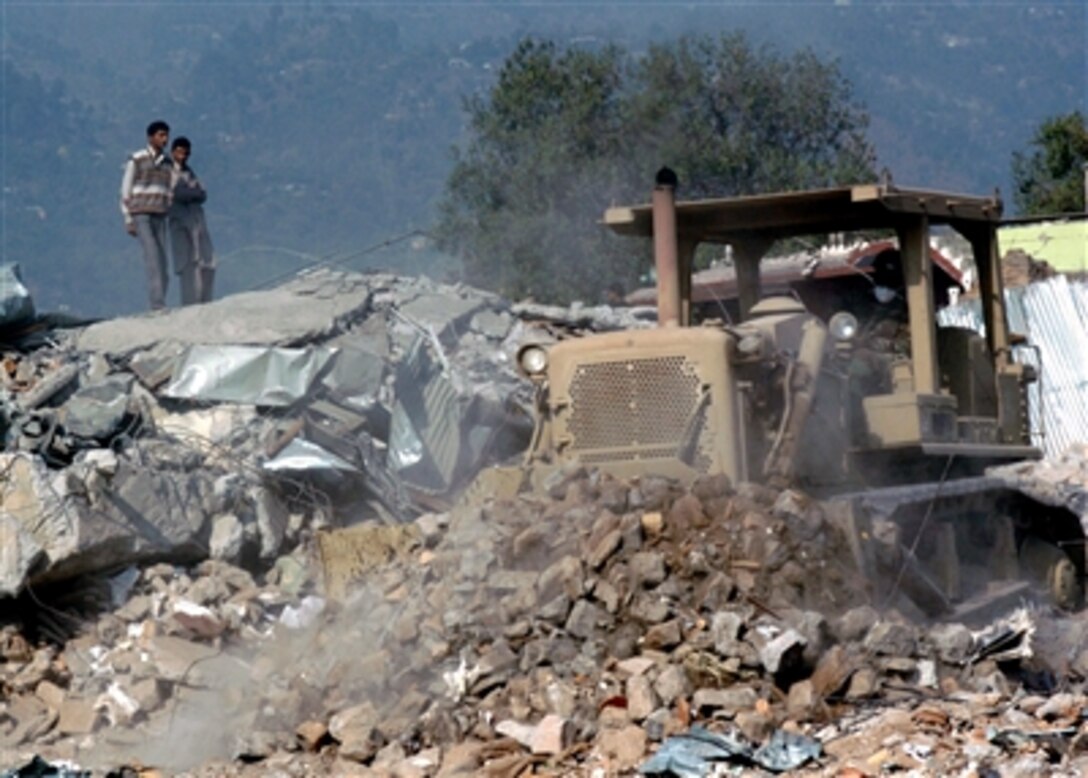 Local Pakistanis watch as U.S. Navy Petty Officer 2nd Class Percy Evans, assigned to Naval Mobile Construction Battalion 74, operates a bulldozer to push debris caused by the Oct. 8 earthquake from the Muzaffarabad Technical University in Muzaffarabad, Pakistan, Nov. 2, 2005. 
 