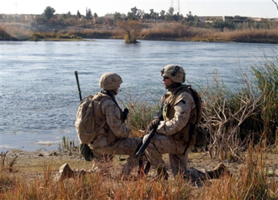 U.S. Marine Corps Lance Cpl. Miez, a radio operator, and Cpl. Brad Adams, both with Lima Company, 3rd Battalion, 1st Marine Regiment, keep watch while on a security halt during a patrol down a riverbed in Barwana, Iraq, Jan. 15, 2006. 