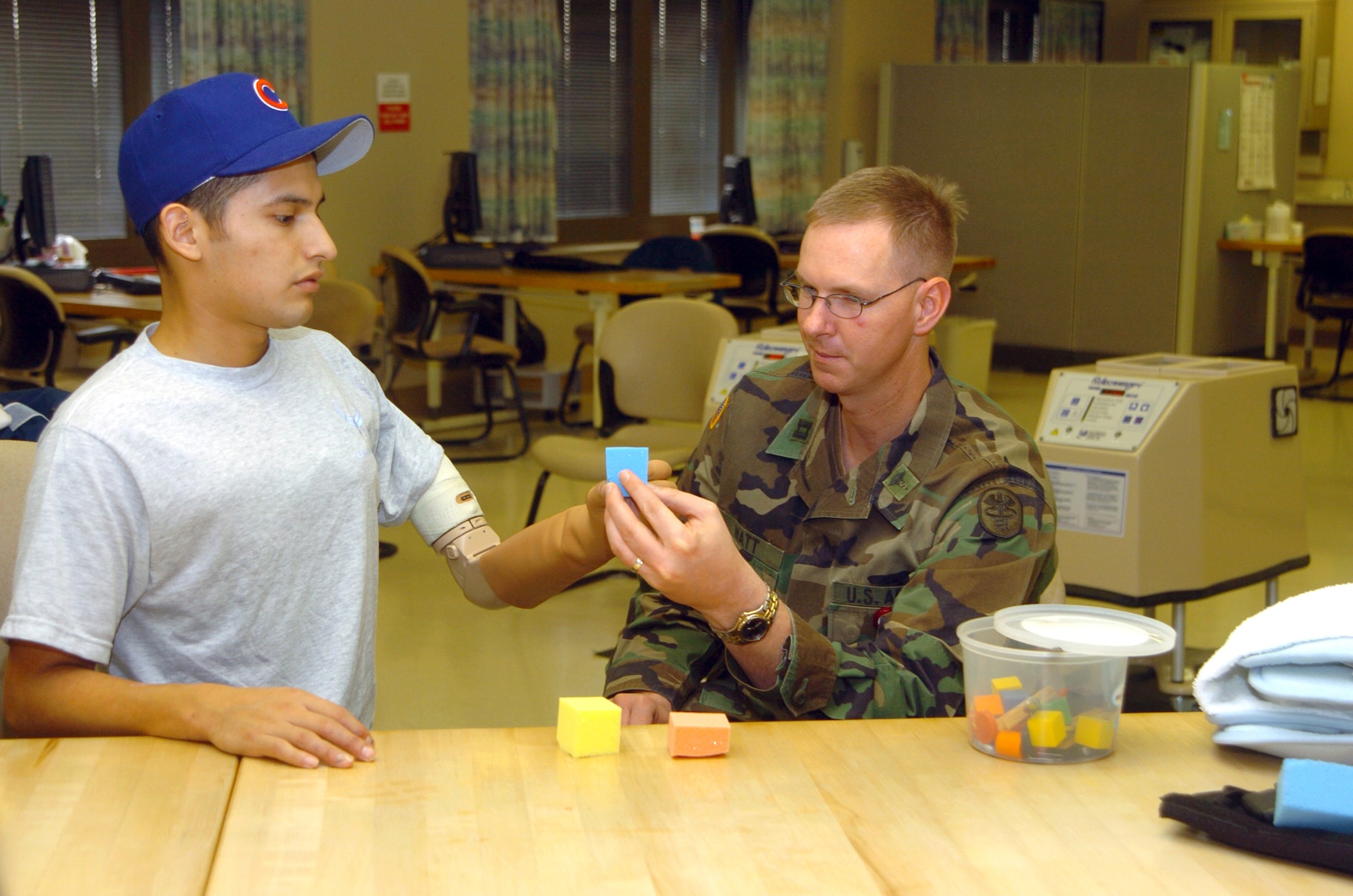 Army Capt. James Watt, an occupational therapist, helps Senior Airman Dan Acosta through some prosthetic arm warm-up drills Thursday, Feb. 23, 2006, in the amputee rehabilitation clinic at Brooke Army Medical Center in San Antonio. (U.S. Air Force photo/Steve White) 