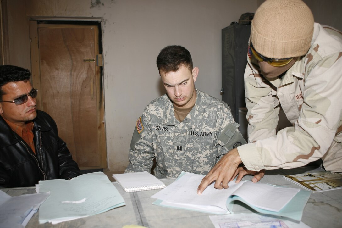 Army Capt. Rob C. Davis, an artillery officer with the 48th Brigade Combat Team assigned to the 2nd Battalion of the 130th Infantry Regiment, listens to ?Alex,? a translator, as he reads Iraqi documents to him in a grievance filed by an Iraqi family. The family?s legal representative, Mohammed, pays attention as the translator deciphers all of the information to Davis. Davis is the civil military officer for the unit responsible for helping Iraqis recover from the hardships that fighting terrorists has brought with it. Davis must compile, translate and organize the information necessary to validate each claim before he can make the condolence payments. So far, the civil military operations program here has worked with U.S. Marine financial disbursers to distribute close to $50,000 in grievances and rewards for information leading to terrorist apprehension. The unit has helped the nearby villages with various humanitarian support projects such as re-supplying the local clinics, food distributions and has even given out soccer nets for playgrounds.