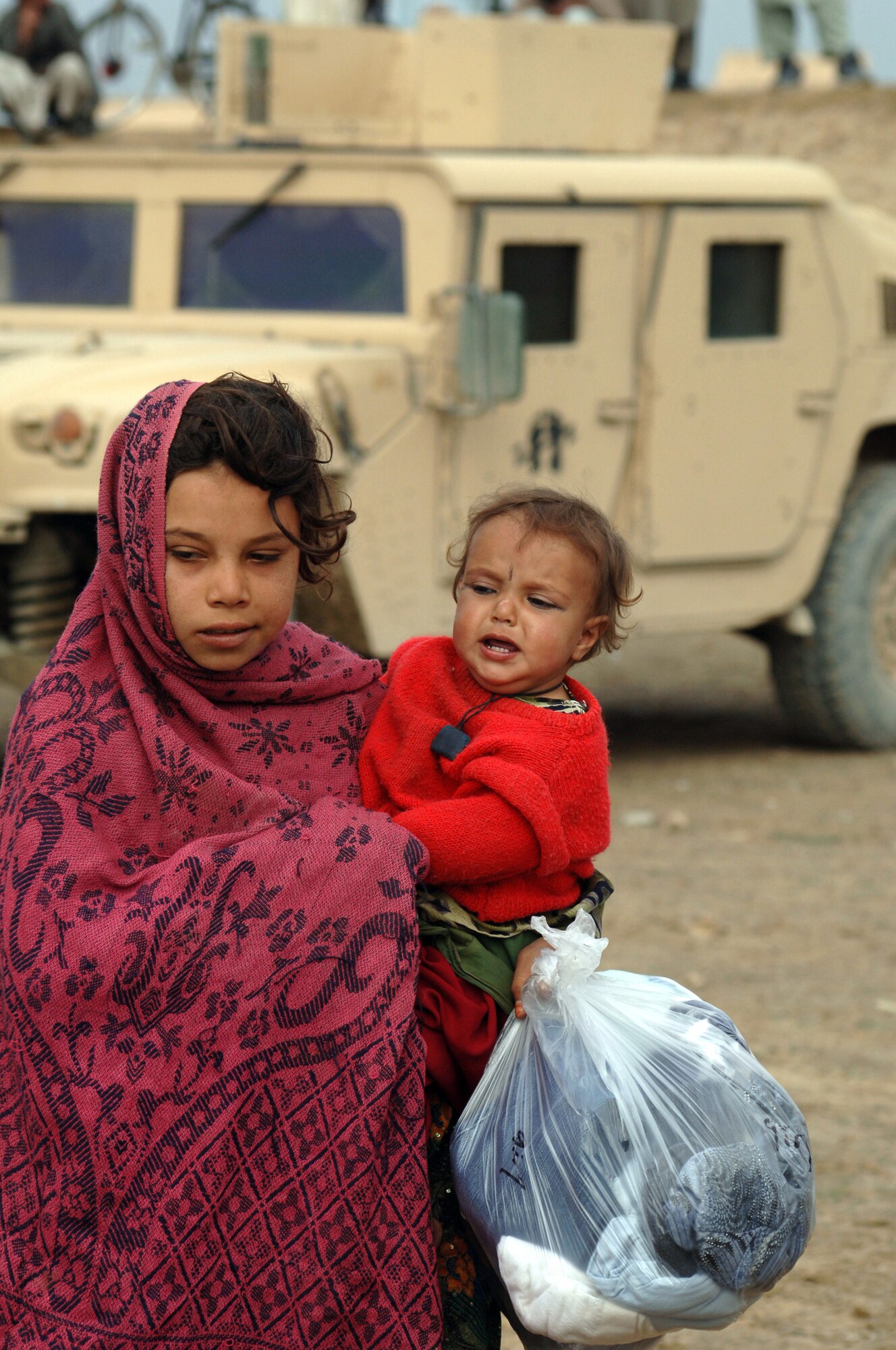 After a rare opportunity of going before men, a young girl carries a bag of clothes to her older sister, who by custom, was not allowed to be photographed. Airmen with the 455th Air Expeditionary Wing recently handed out more than 400 bags of clothes, shoes, school supplies, hygiene items and toys to the residents of the village of Gadia in Parwan Province, Afghanistan. (U.S. Air Force photo/Staff Sgt. Jennifer Redente) 