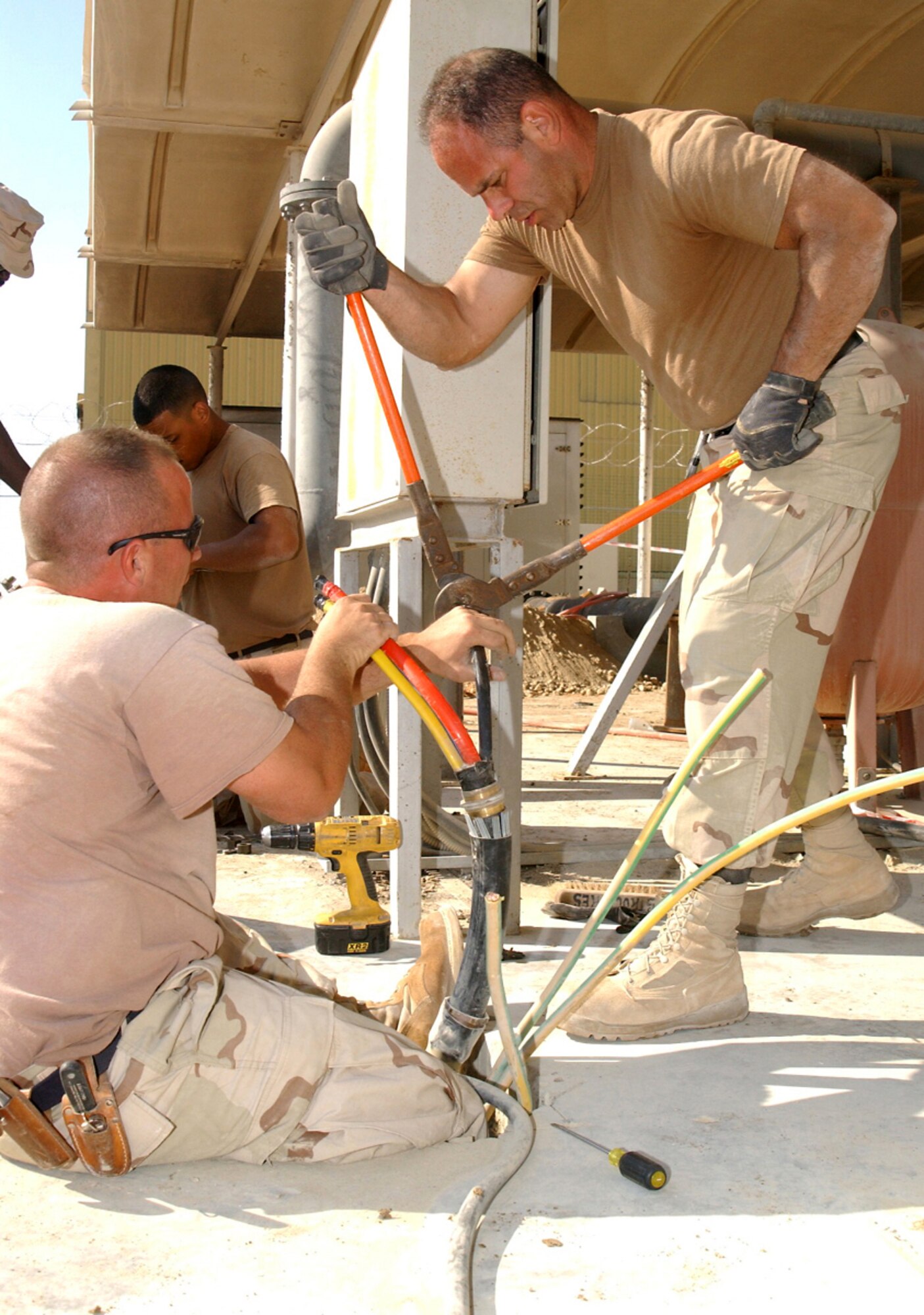 Senior Airman John Quaioto cuts a main lead to the proper length while Tech. Sgt. John Fenwick helps hold the wires at a deployed location in Southwest Asia. The two work in the 380th Expeditionary Civil Engineer Squadron electrical shop and were installing an automatic switch between a backup generator and commercial power near the flightline. (U. S. Air Force photo/Tech. Sgt. Andrew Leonhard)