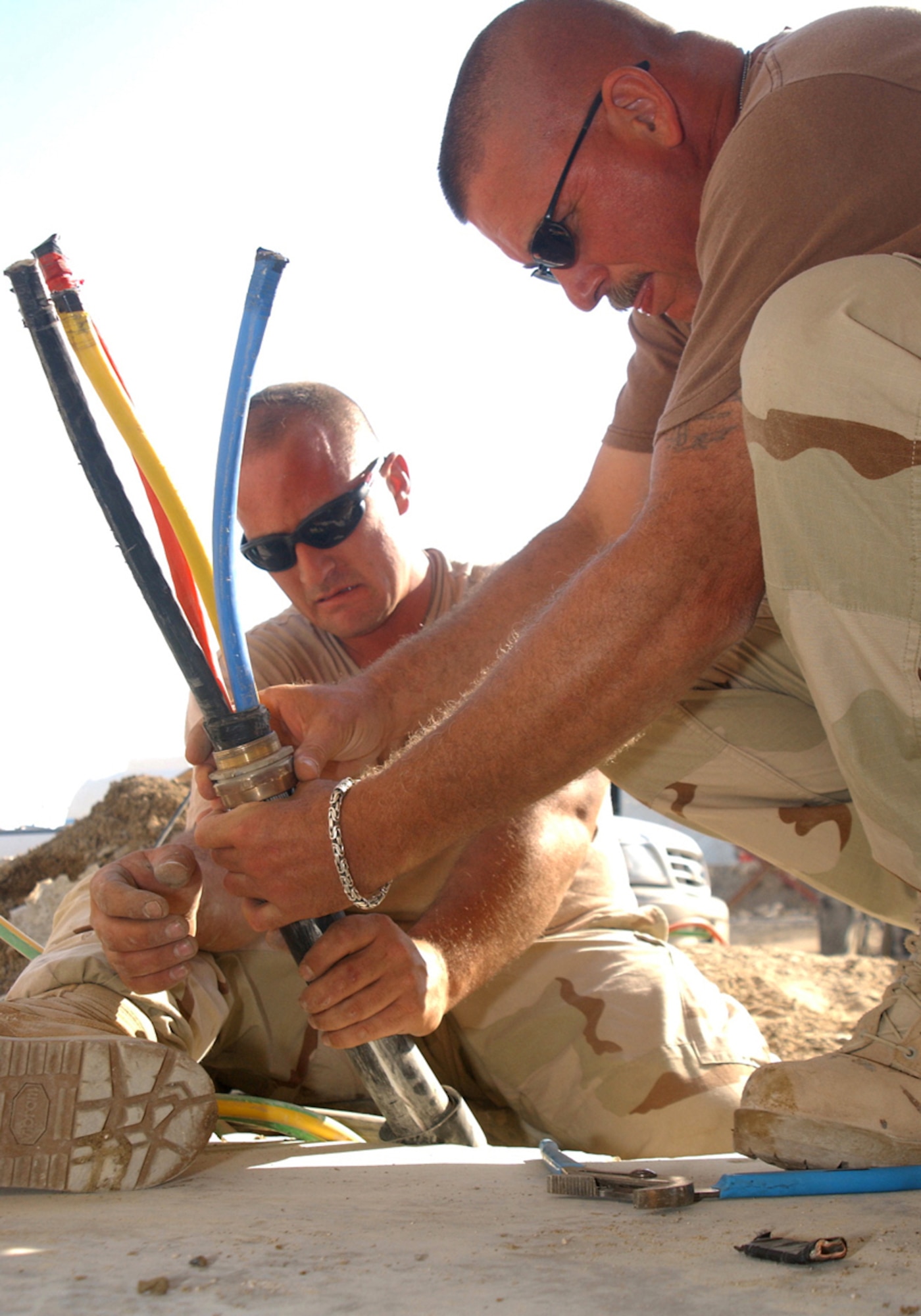 Master Sgt. Brian Ross (right) and Tech. Sgt. John Fenwick install a coupling onto a main lead between an automatic switch and a generator at a deployed location in Southwest Asia. The Airmen are with the 380th Expeditionary Civil Engineer Squadron electrical shop. (U.S. Air Force photo/Tech. Sgt. Andrew Leonhard)


