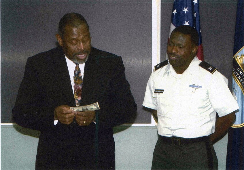 HANSCOM AIR FORCE BASE, Mass. - Retired Chief Master Sgt. Walter Richardson give back a dollar bill to his son, Col. Richardson, at the colonel's promotion ceremony. This was the same dollar the colonel presented his father for giving him his first salute in 1977. (Photo courtesy of Chief Richardson)

