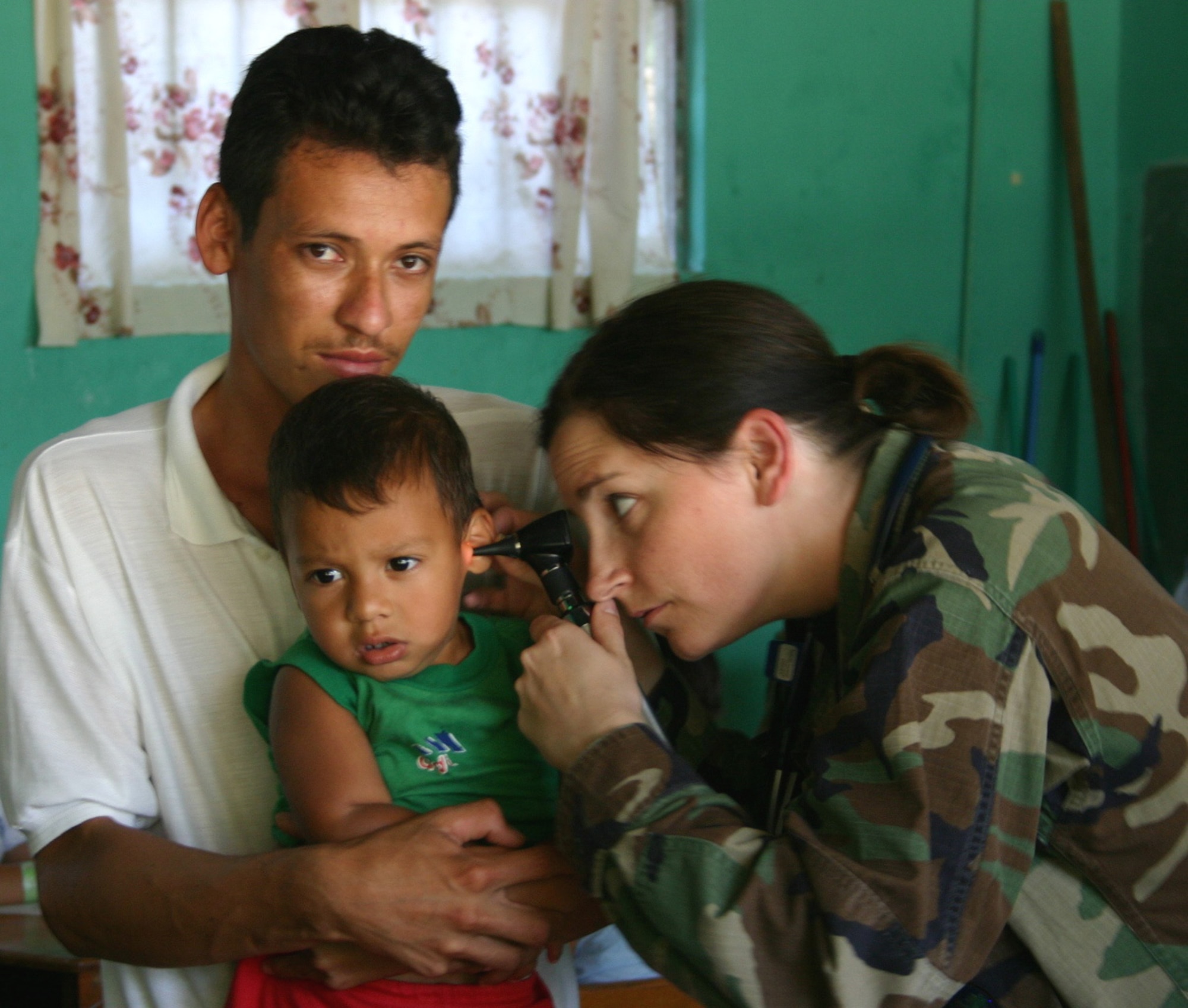 A man holds his son as Maj. (Dr.) Jamie Glover, a family practice physician from the 96th Medical Operations Squadron at Eglin Air Force Base, Fla., examines the boy's ear. A team of medics are conducting the two-week medical readiness training exercise, or MEDRETE, in association with the New Horizons 2006-Honduras exercise. (U.S. Air Force photo/Capt. Mike Chillstrom)