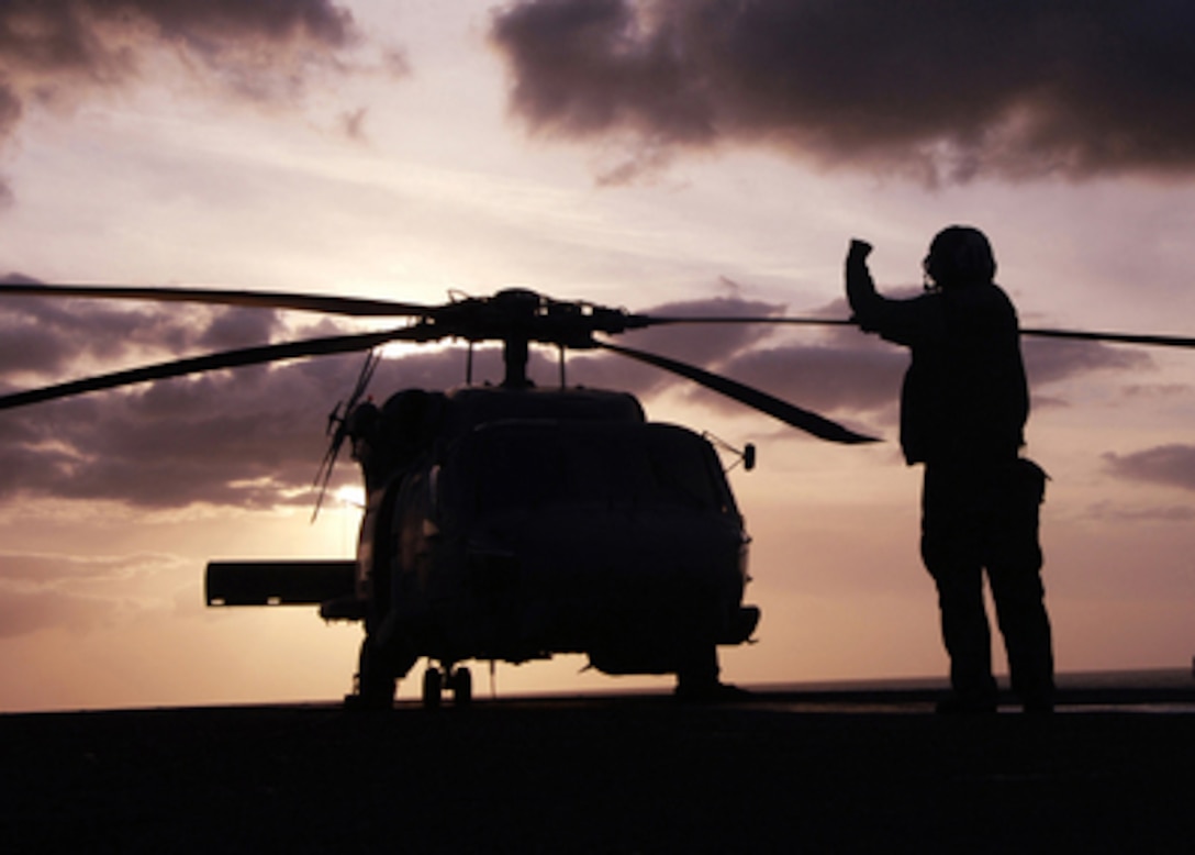A flight deck crewman signals to the pilots of an MH-60 Seahawk helicopter to starts its engines at the beginning of flight operations aboard the aircraft carrier USS George Washington (CVN 73) on March 9, 2006. The George Washington is conducting carrier qualifications and shipboard training in the Atlantic Ocean. The Seahawk is assigned to Helicopter Sea Combat Squadron 28. 