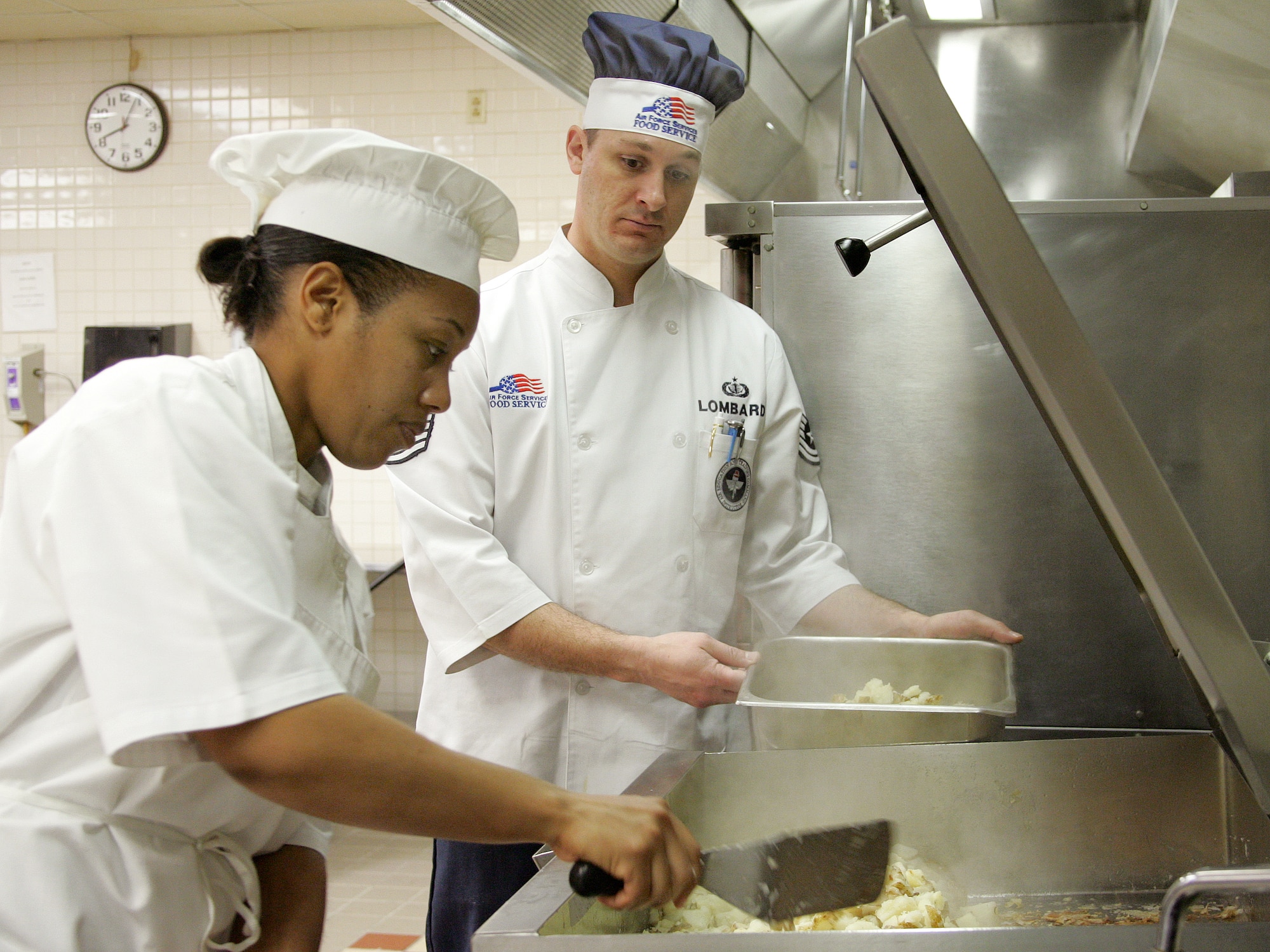 Senior Airman Crystal Radcliff "pans-up" cottage fried potatoes as her instructor, Tech. Sgt. Richard Lombardi, oversees her progress on Monday, March 13, 2006.  Airman Radcliff is a services student at the Culinary Arts Training Center at Lackland Air Force Base, Texas. (U.S. Air Force photo/Robbin Cresswell)