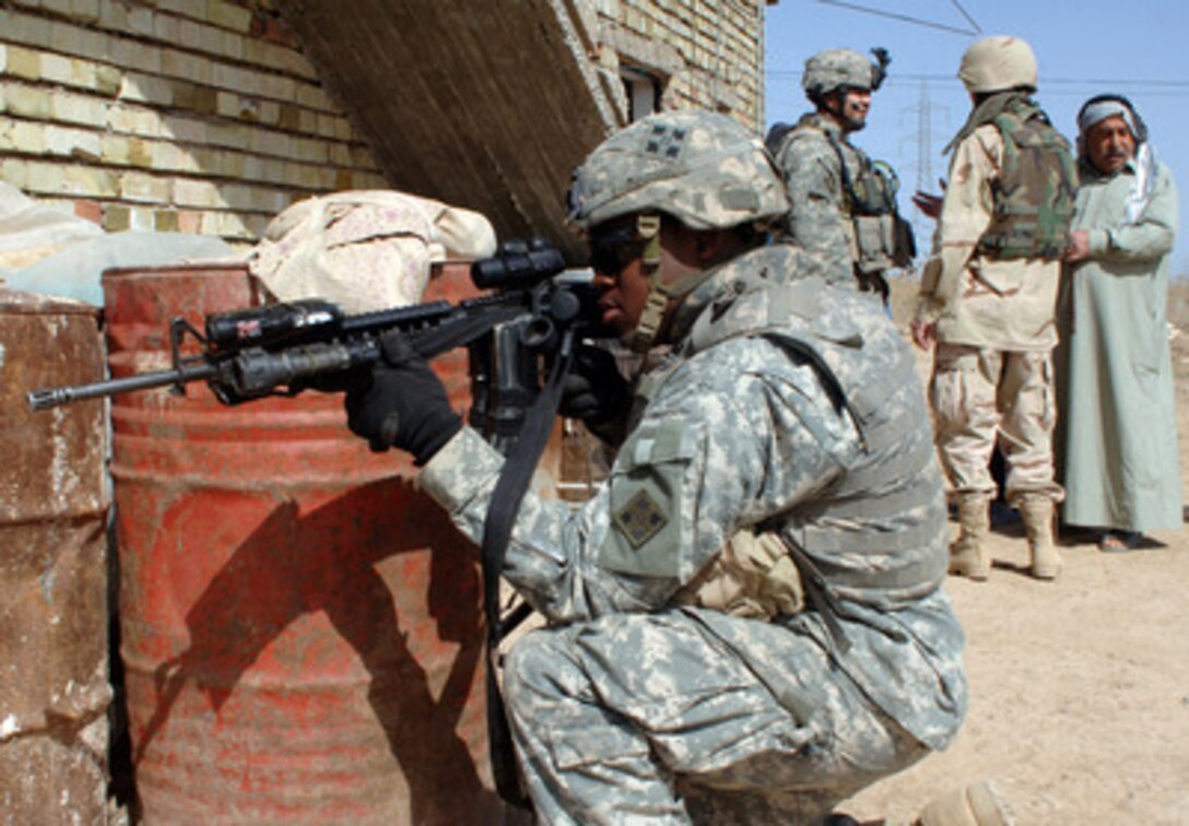 Army Pfc. Jonathan Dixon (foreground) provides perimeter security while Staff Sgt. Gabriel Monreal and his translator conduct an interview with a local Iraqi man during a routine patrol near Camp Taji, Iraq, on March 13, 2006. Dixon and Monreal are attached to Alpha Company, 1st Battalion, 66th Armored Regiment. 