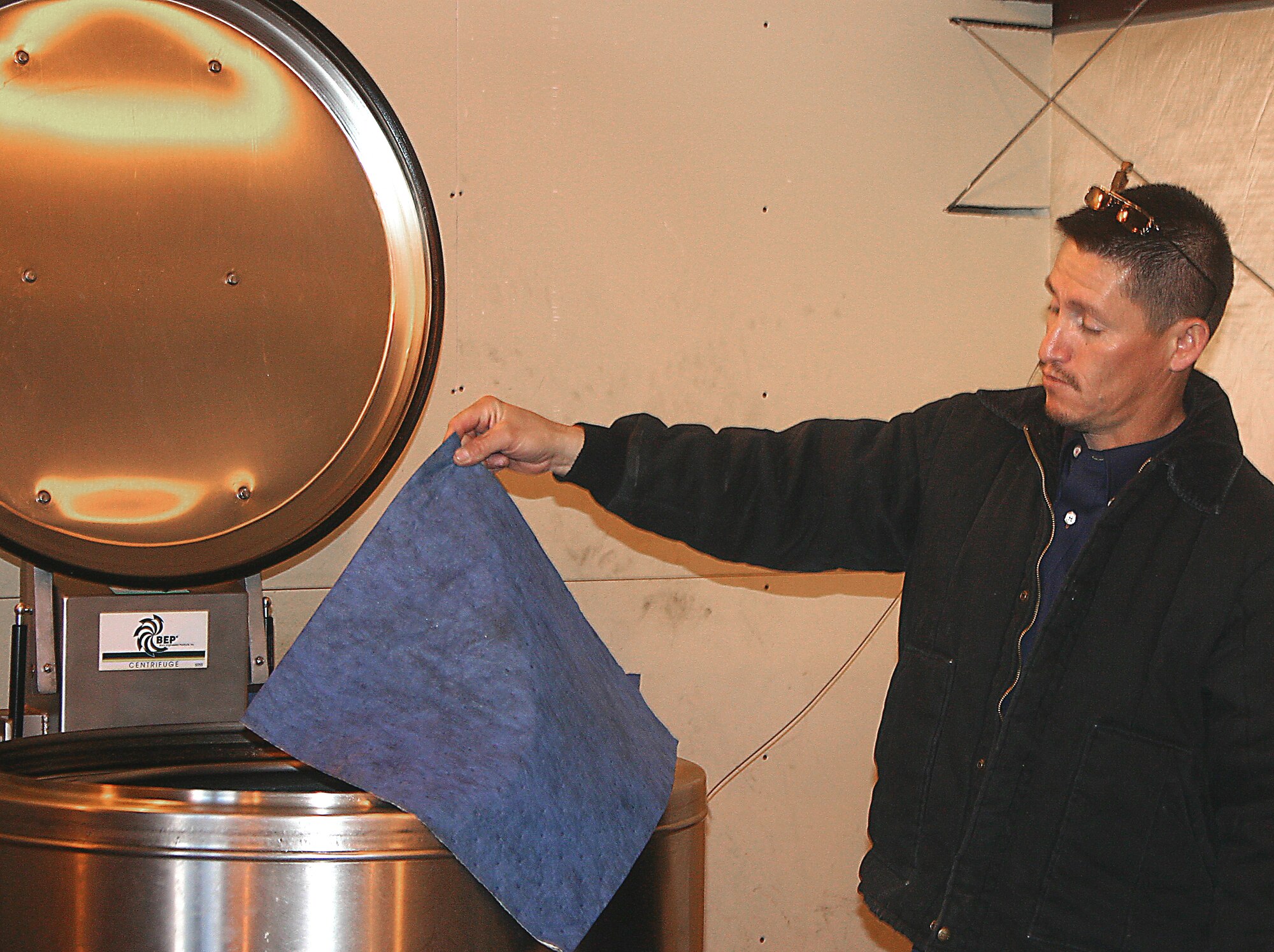 CANNON AIR FORCE BASE, N.M. -- Jake Madril, 27th Civil Engineer Squadron, explains how oily rags are run through a centrifuge. The oil is sold and the rag is reused, saving Cannon money and reducing pollution. (U.S. Air Force photo by Janet Taylor-Birkey)
