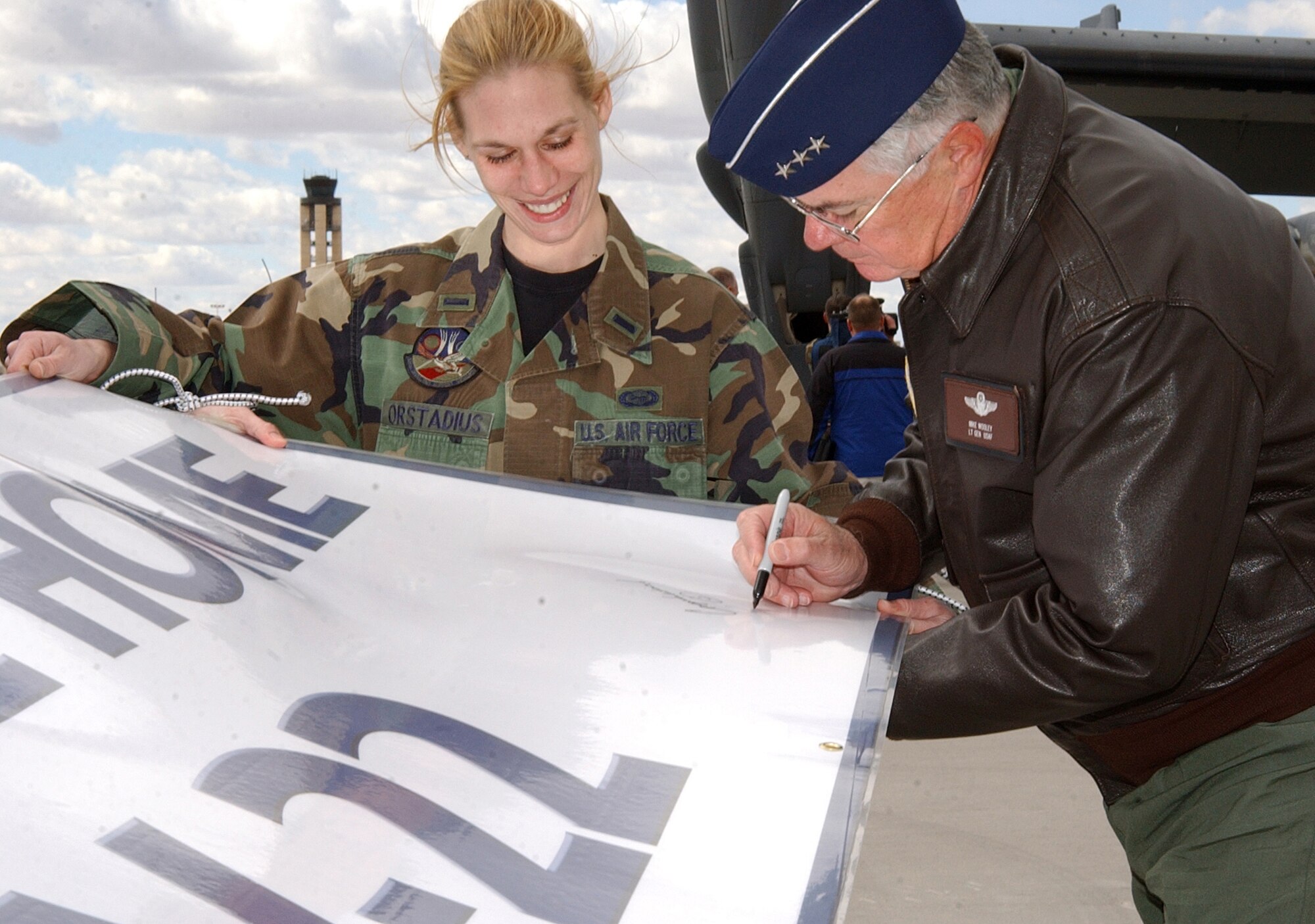 1st Lt. Anna Orstadius steadies a welcome banner while Lt. Gen. Mike Wooley, autographs it at Kirtland Air Force Base, N.M, after the first CV-22 Osprey arrived at the base Monday, March 20, 2006. General Wooley is commander of Air Force Special Operations Command. Lieutenant Orstadius is with the 58th Operational Support Squadron. (U.S. Air Force photo/Staff Sgt. Markus Maier)