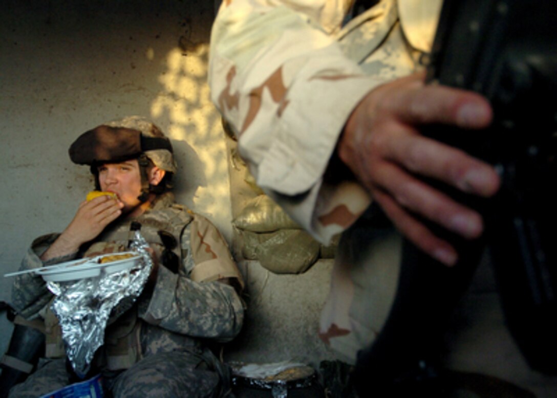 U.S. Army Pfc. Brandon Standifer eats dinner during his shift in a guard shack as another soldier keeps watch at Camp Taji, Iraq, on March 19, 2006. 