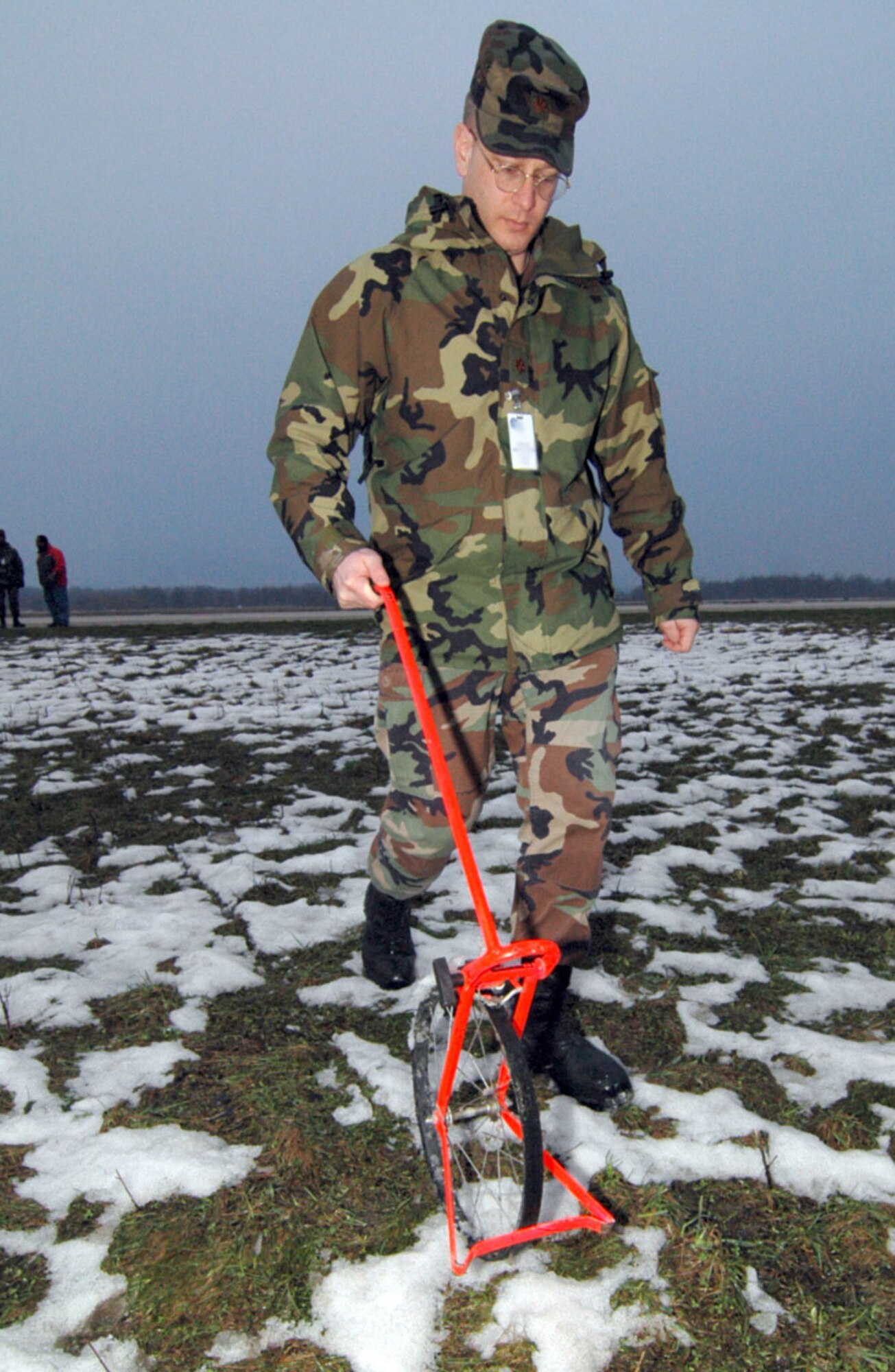 Maj. Louis Lilley uses a measuring wheel to determine the distance between the taxiway center line and suspected obstructions, in this case tree lines, as part of the waiver package at Tuzla Air Base.
