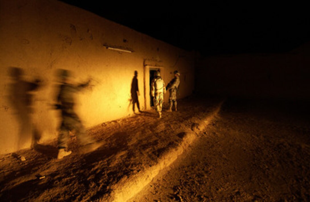 U.S. Army and Iraqi army soldiers are bathed in the headlights of vehicles as they approach the doorway of a house during a combat patrol in Sighar, Iraq, on March 25, 2006. Soldiers from the 1st Brigade, 1st Armored Division are conducting joint patrols with Iraqi soldiers in Sighar. 