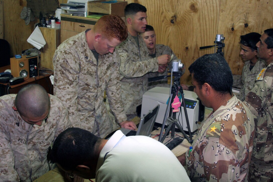 Cpl. Alexander Villada, a Miami native, (left), checks over a soldier's vehicle registration form while Cpl. Travis C. Adams, an Anaheim, Calif., native, (middle), prepares to log it into a computer at Al Asad, Iraq, March 27. Both Marines are badging shift leaders with the Badging Office, Provost Marshal's Office, 1st Battalion, 109th Mechanized Infantry, Marine Wing Support Group 37 (Reinforced), 3rd Marine Aircraft Wing.