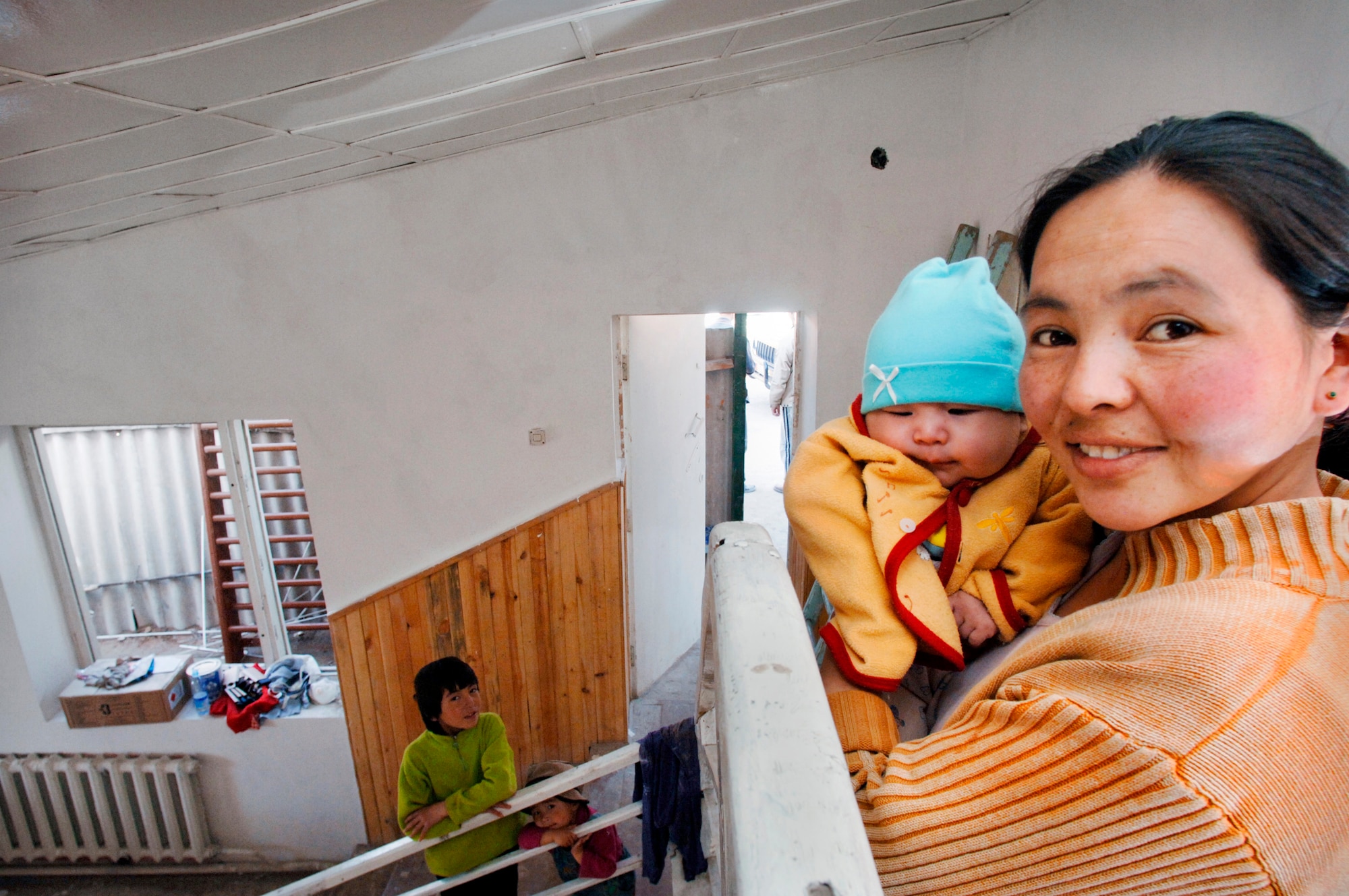 Shirin Aroonova stands on the second floor landing to look at the work completed by volunteers on Sunday, March 12, 2006. Her children are 3-month-old Isman, 3-year-old IzLam and 12-year-old Meerim. When the home reopens, her husband and family will be the staff and caretakers of the children's home and physical therapy center. (U.S. Air Force photo/Master Sgt. Lance Cheung) 