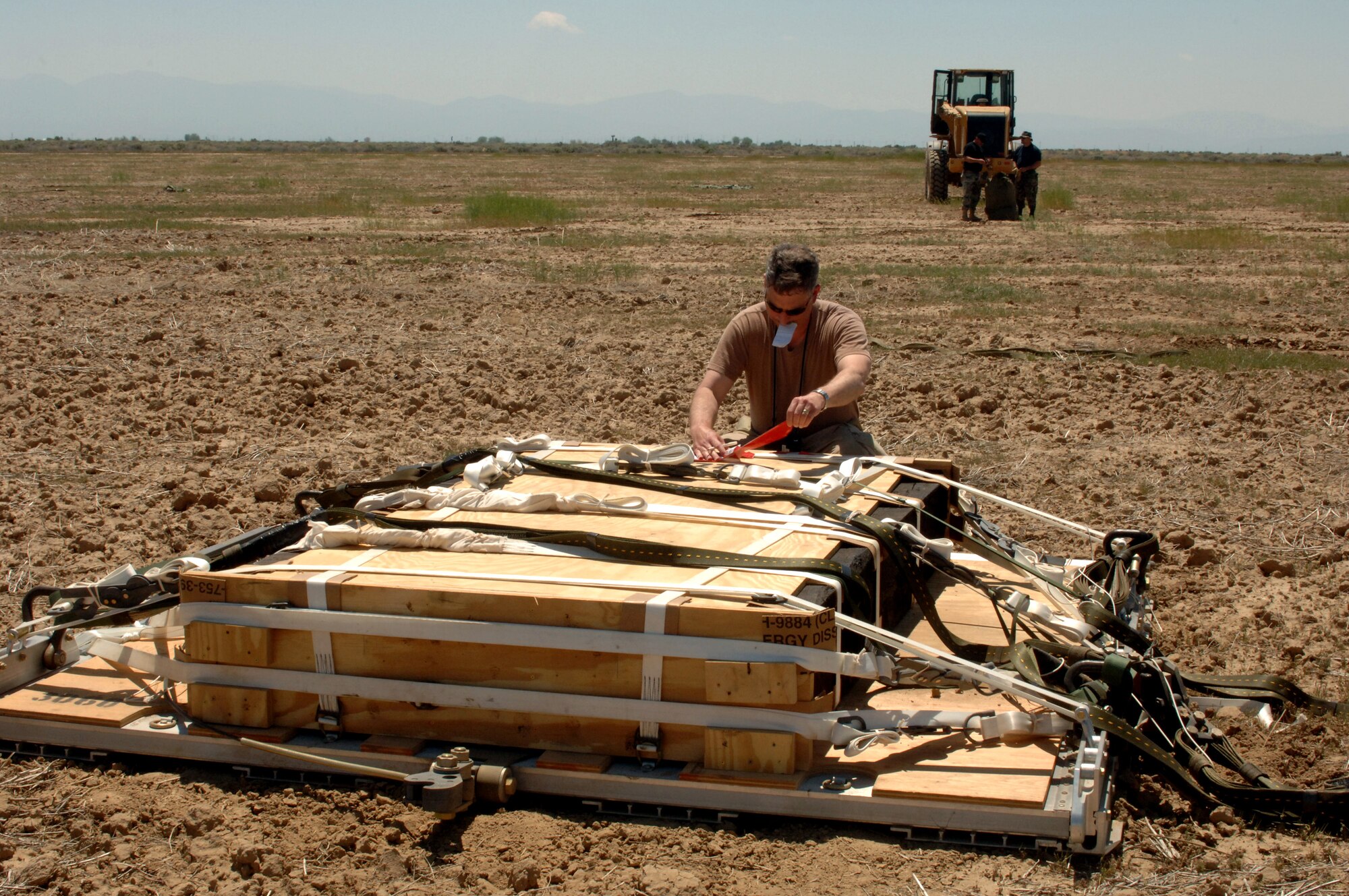 Lt. Col. Arvin Mayberry checks the tag on a Type 5 heavy pallet that was extracted from a C-130J Hercules on Sunday, April 30, 2006. Two Airmen in the background pack the parachute which pulled the pallet from the aircraft. Guard, Reserve and active-duty aircrews from Channel Islands Air National Guard Base, Calif.; Little Rock AFB, Ark.; and Keesler AFB, Miss., participated in the mission which tested the aircraft's capability to drop this type of pallet. This was the first time the "J" model dropped a Type 5 pallet. Colonel Mayberry is with the 115th Airlift Squadron at Channel Islands ANGB. (U.S. Air Force photo/Tech. Sgt. Dave Buttner)