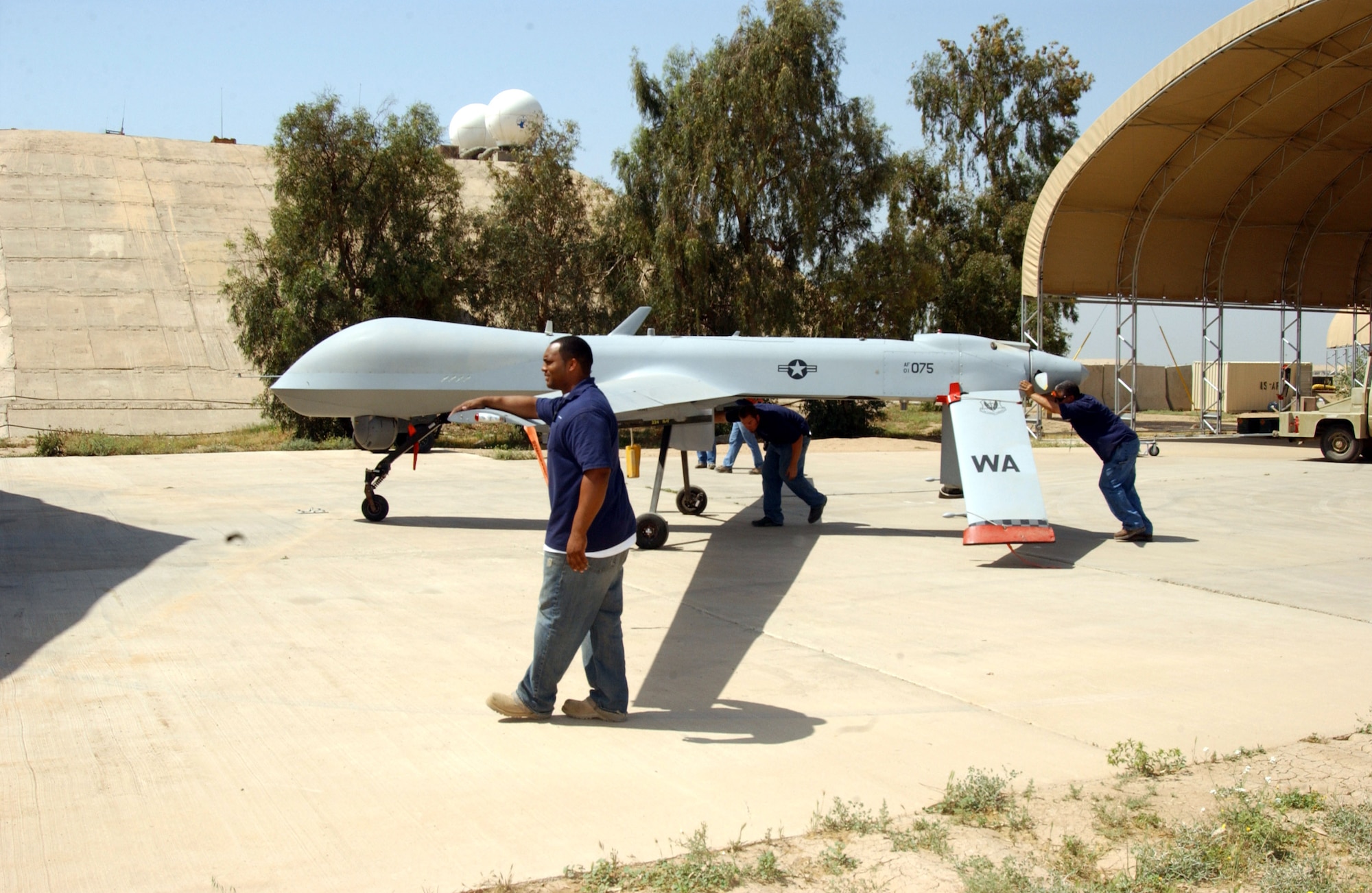 Three contract maintainers walk an RQ-1 Predator unmanned aerial vehicle into a shelter. They are assigned to the 46th Expeditionary Aircraft Maintenance Unit at Balad Air Base, Iraq. (U.S. Air Force photo/Airman 1st Class Jason Ridder) 
