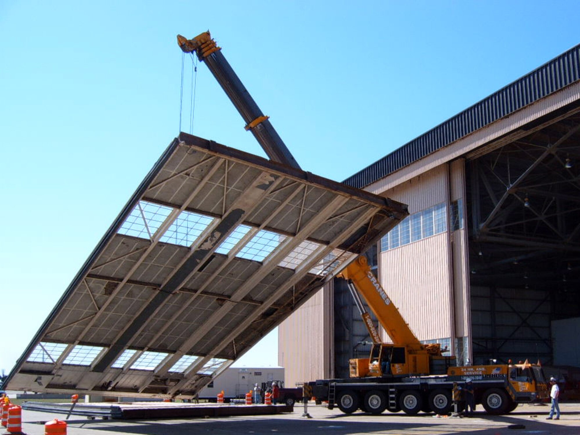 A crane lowers one of the original Eason Hangar doors to the ground as part of phase 1 repairs.  The hangar was built in 1957 and was heavily damaged from recent hurricanes.  All 16 doors will be replaced by the end of the year along with other modifications.