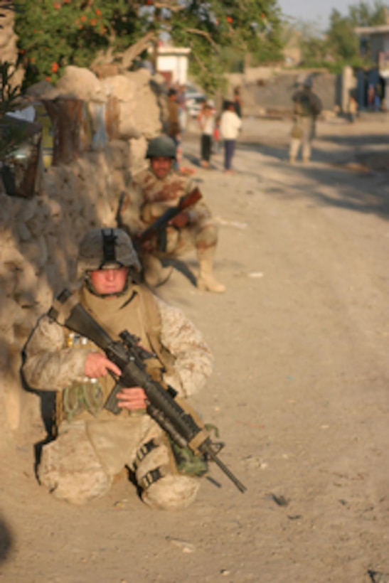 A U.S. Marine and an Iraqi army soldier kneel along a wall as they keep watch over a road during a patrol in Al Ish, Iraq, on April 27, 2006. The Marine is attached to Weapons Company, 1st Battalion, 7th Marines Regiment. 