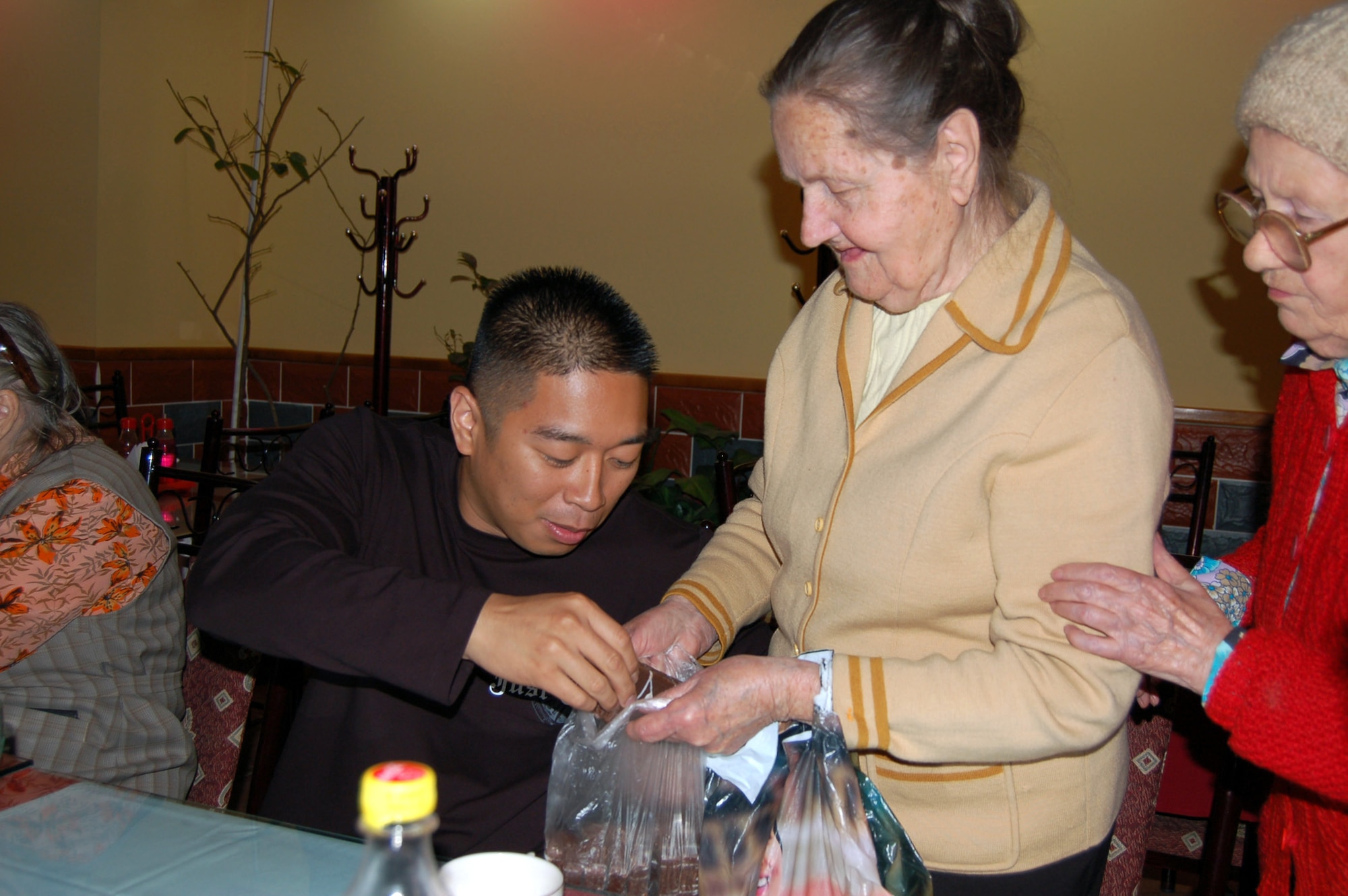 A babushka shares treats with Staff Sgt. Edwin Mirador and other Airmen from nearby Manas Air Base after lunch in Bishkek, Kyrgyzstan, on Thursday, May 4, 2006. The babushkas enjoy sharing treats they make themselves. Airmen from nearby Manas Air Base sponsor 20 elderly women who receive aid from Babushka Adoption. The local non-governmental organization assists elderly people left vulnerable as this post-Soviet nation works to stabilize its economy. Sergeant Mirador is deployed from Barksdale Air Force Base, La. (U.S. Air Force photo/Staff Sgt. Lara Gale)