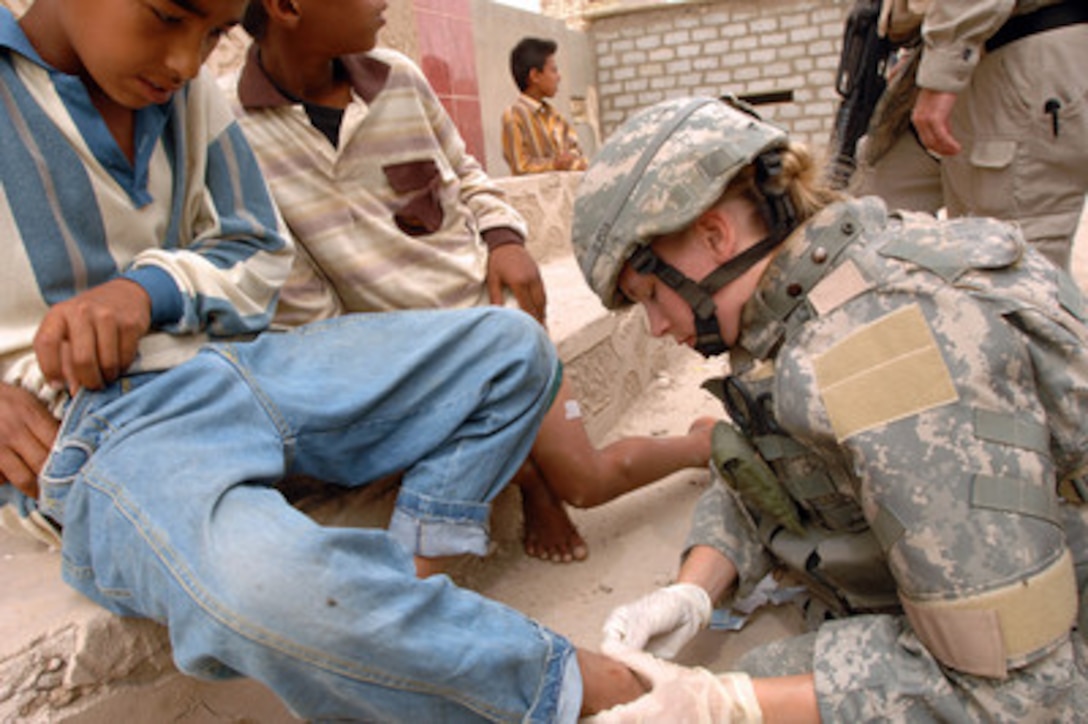 U.S. Army Pfc. Corione Woods cleans an open wound on an Iraqi child's leg outside the Al-Nasar Welsalem police station in Baghdad, Iraq, on May 4, 2006. Woods is treating the boy's leg during a joint neighborhood patrol with Iraqi army soldiers. 