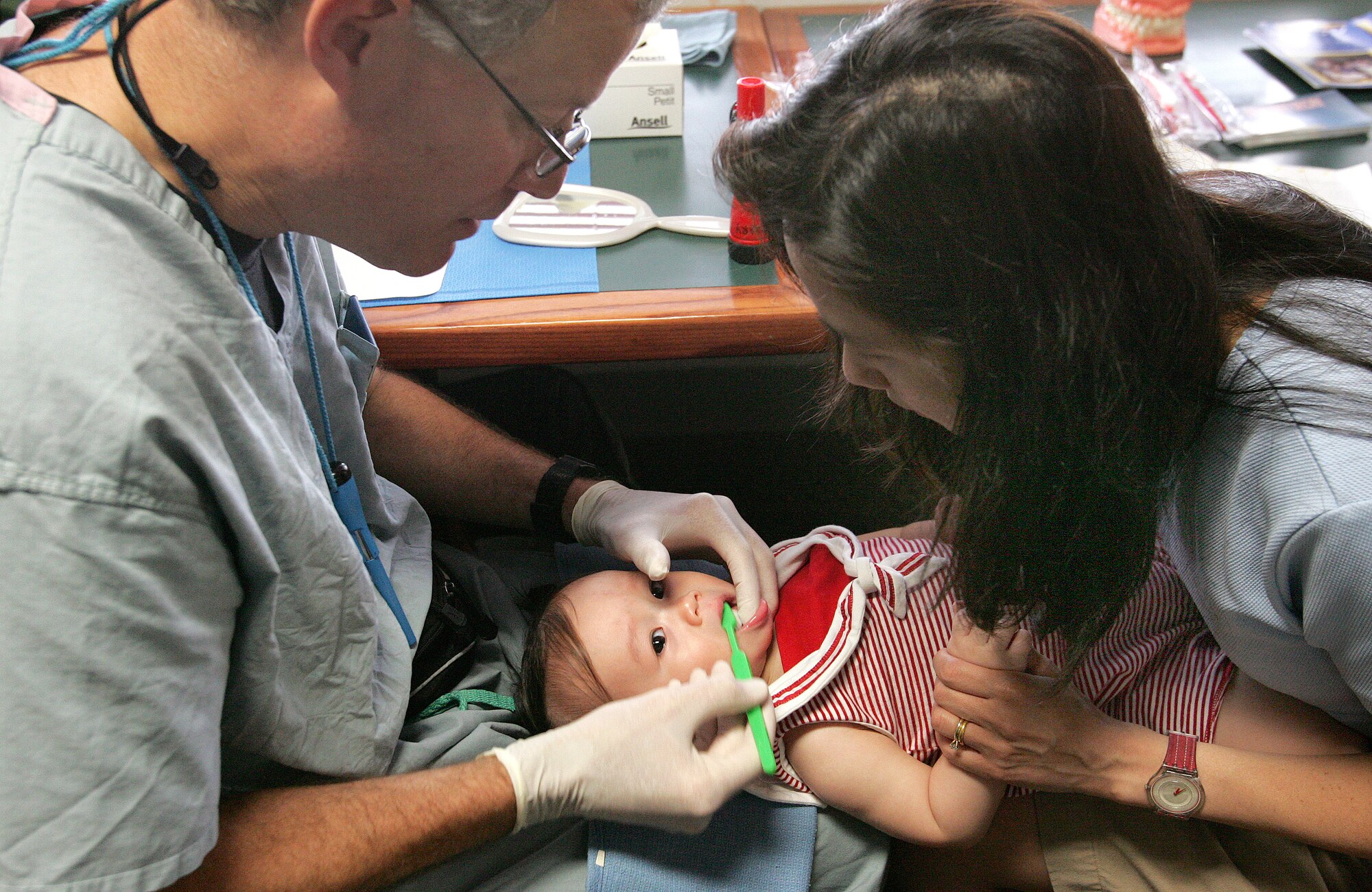 Elena Nguyen holds her daughter, Lien-Huong, while Col. (Dr.) Jeffery Mabry brushes the infant's teeth at the Skylark Community Center at Lackland Air Force Base, Texas, on Wednesday, May 10, 2006. The pediatric dental department at Lackland provides drop-in dental screening as part of their pediatric dental training program. Colonel Mabry is director of pediatric dentistry with the 59th Dental Squadron. (U.S. Air Force photo/Robbin Cresswell)