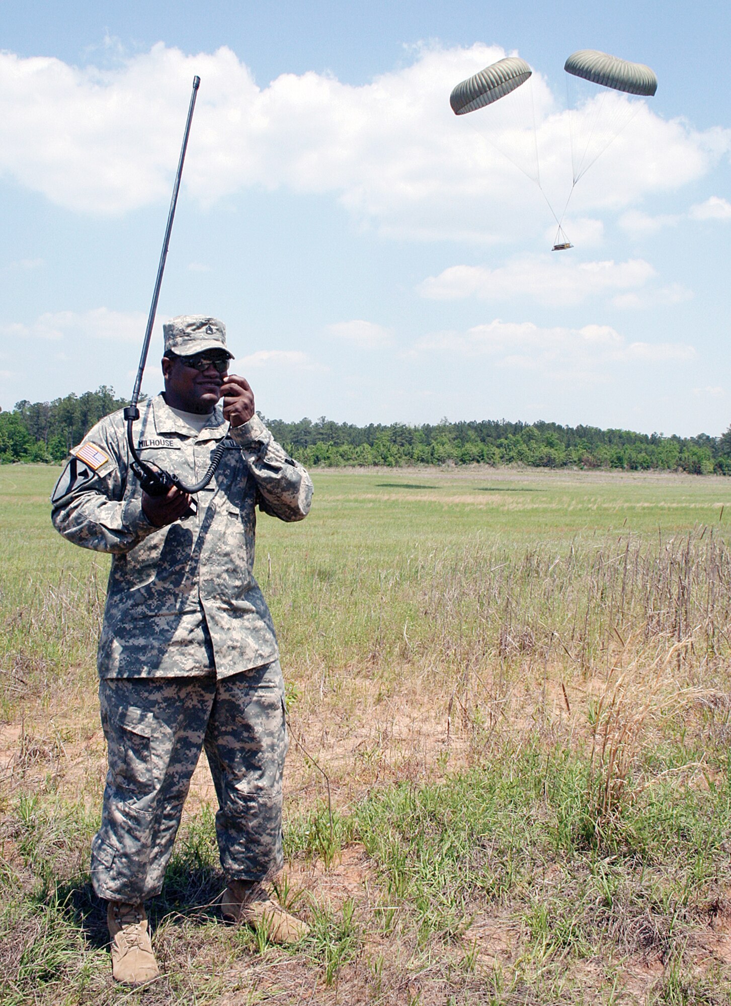 Army Staff Sgt. Andre Milhouse of the 551st Signal Battalion communicates with a C-130 Hercules crew from the 700th Airlift Squadron out of Dobbins Air Reserve Base, Ga., as airdropped cargo comes down behind him. The joint training is the first of its kind at Fort Gordon, Ga., and will be added to the final capstone event of Army communications technical training at Fort Gordon. (U.S. Army photo/Kristy Davies)