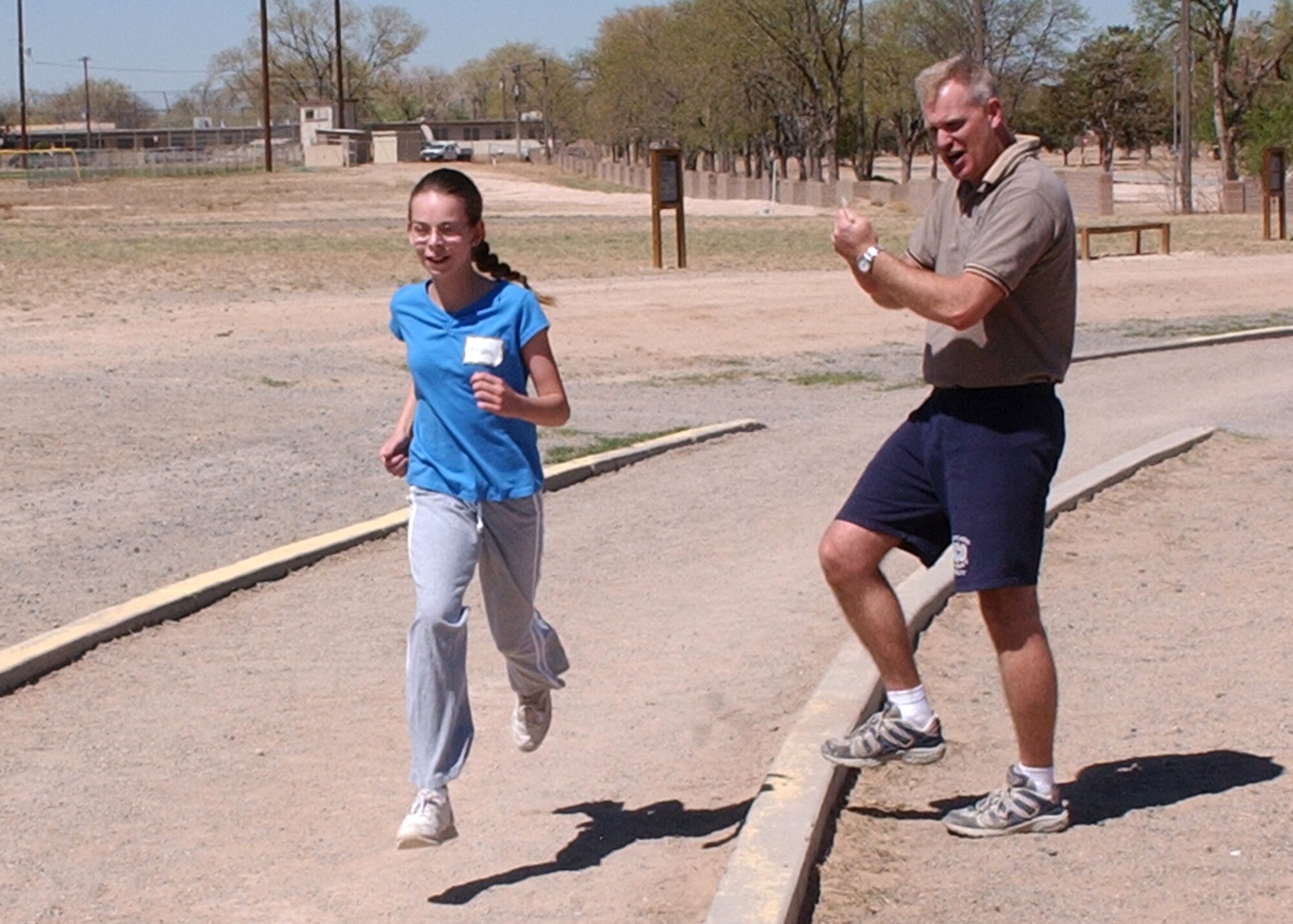 KIRTLAND AIR FORCE BASE, N.M. - Tech. Sgt. Matt Moore of Kirtland's NCO Academy, cheers Megan Norris along during her mile run. Megan ran the fastest girl's time at the event in approximately 7 minutes. (Air Force photo by Dennis Carlson)          