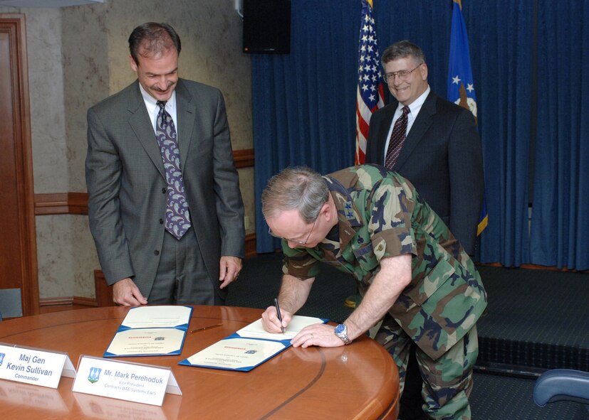 HILL AIR FORCE BASE, Utah - Maj. Gen. Kevin Sullivan, Ogden Air Logistics Center commander, signs the BAE Systems partnership agreement May 11 at Hill Air Force, Base Utah. At left, Mark Perehoduk, vice president for contracts at BAE Systems, awaits his turn to sign the document. In back is BAE Systems Jeff Cook, vice president for readiness and sustainment. (Air Force photo by Carl Burnett)

