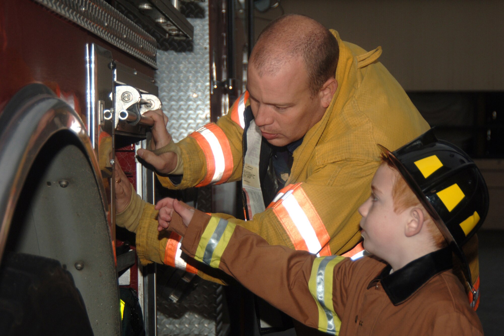 HANSCOM AIR FORCE BASE, Mass. — Eric Naylor, firefighter, provides Jacob Larwood a close-up look at the fire truck. Jacob was named the Grand Marshal of Fire Prevention Week 2004. In 2005, he was made an honorary firefighter. (Air Force photo by Linda LaBonte Britt)