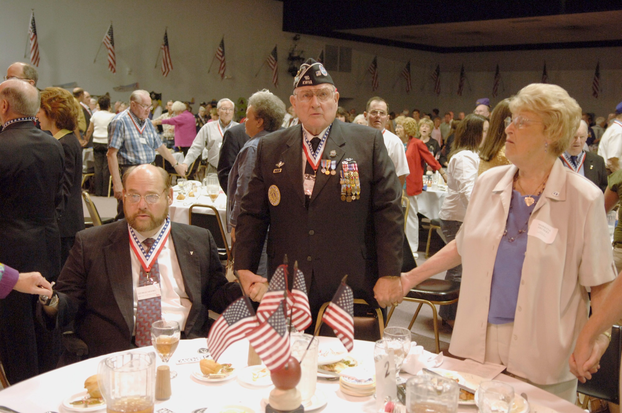 Louis Dechert (standing) and his wife, Marietta, join hands with George Moore as they sing "God Bless America" to close out the 2006 Former POW/Purple Heart Luncheon at Barksdale Air Force Base, La., on Saturday, May 20, 2006.  Eighty-two former prisoners of war and 250 Purple Heart recipients attended.  The keynote speaker was Lt. Gen. Kevin P. Chilton, 8th Air Force commander.  Mr. Dechert is the national president of the Korean War Veterans Association; Mr. Moore is director of the Overton Brooks VA Medical Center in Shreveport, La. (U.S. Air Force photo/Master Sgt. Michael A. Kaplan) 