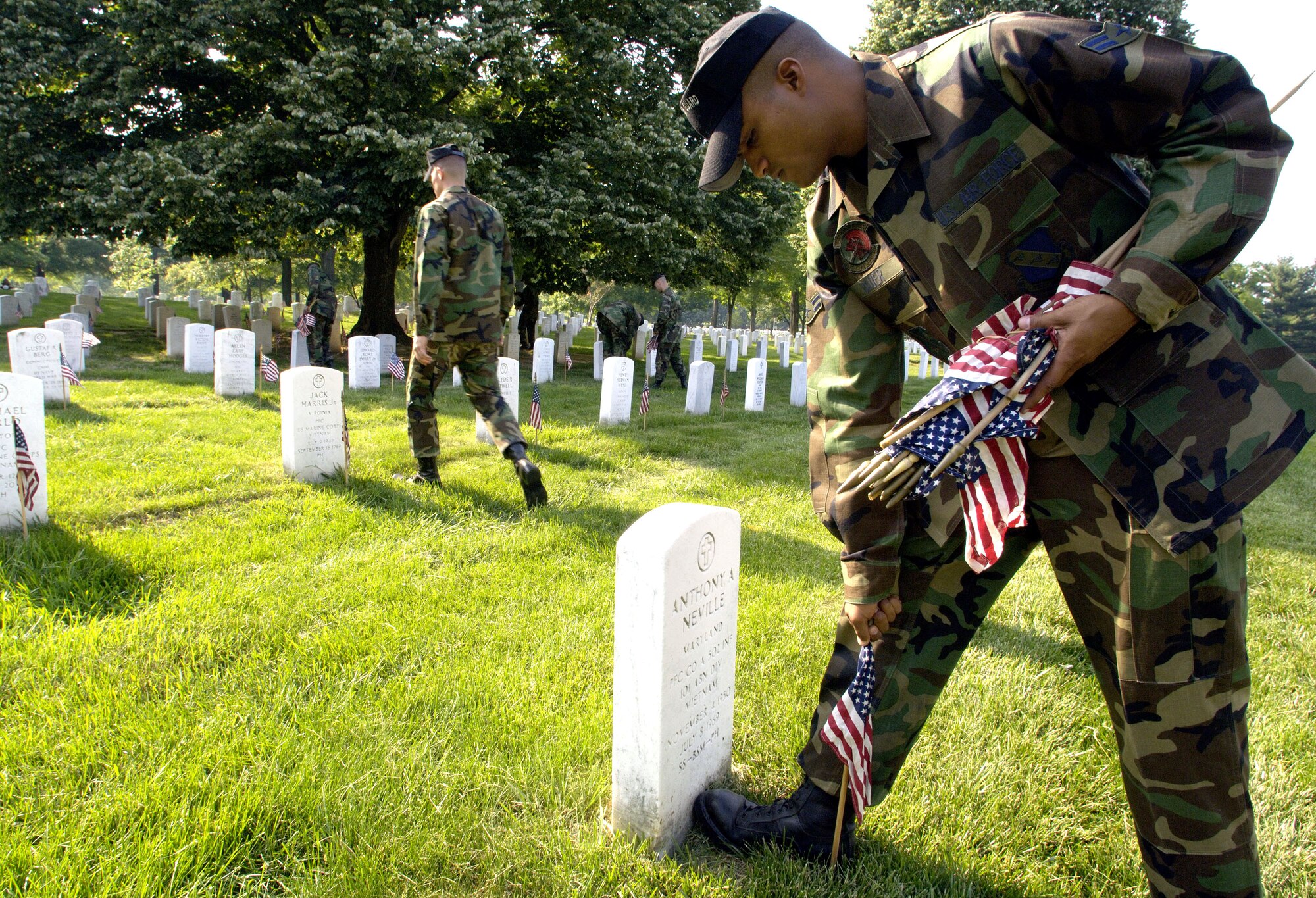 A member of the United States Air Force Honor Guard Drill Team places a flag in front of a headstone at Arlington National Cemetery on Thursday, May 25, 2006. Assigned to Bolling Air Force Base, Washington D.C., he joined hundreds of Soldiers, Sailors, Airmen and Marines from across the Washington D.C. area to place more than 227,000 flags at the front of headstones. The flags will remain at the headstones through Memorial Day. (U.S. Air Force photo/Master Sgt. Jim Varhegyi)