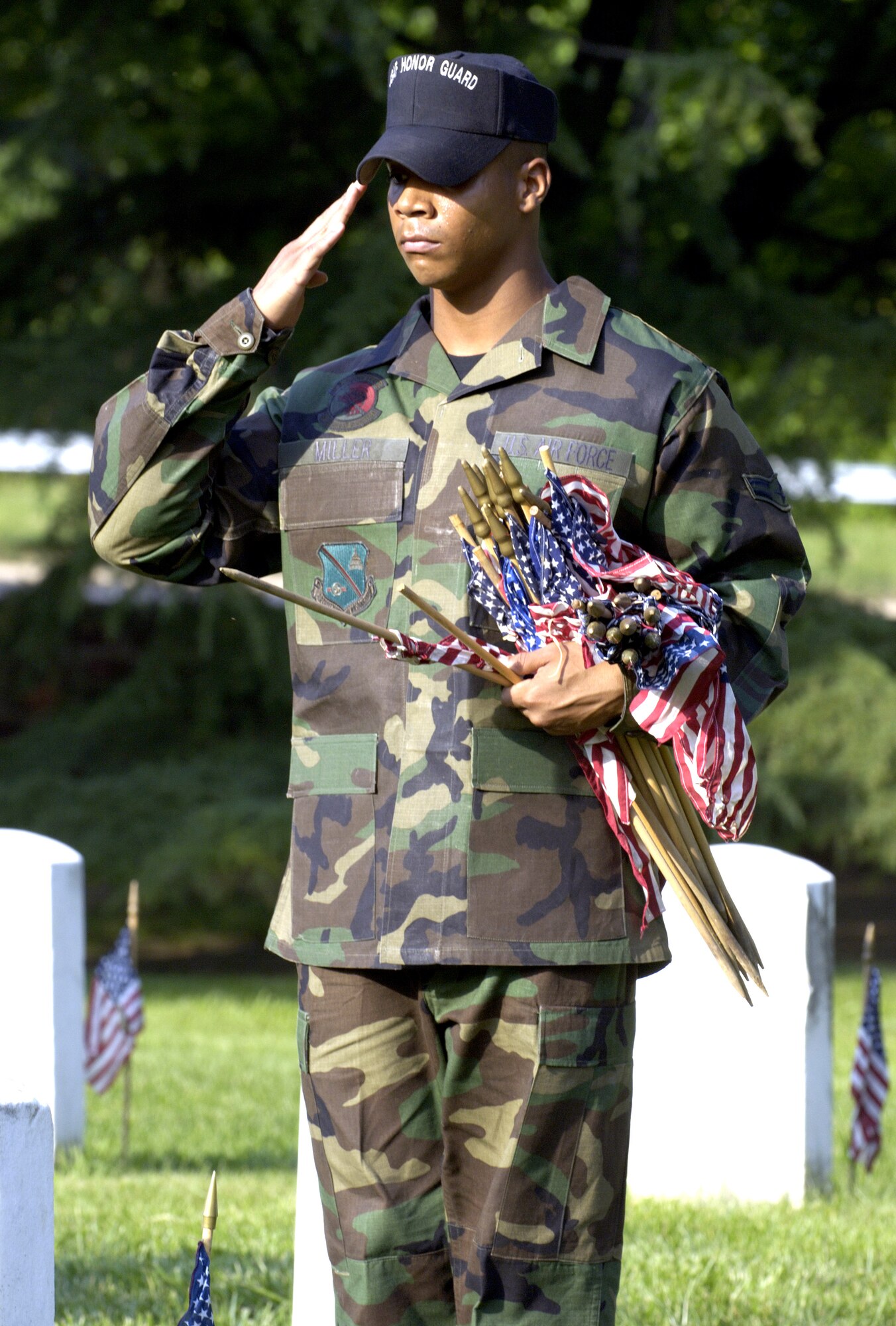 Airman 1st Class Darrell Miller renders honors after placing a flag in front of a headstone at Arlington National Cemetery on Thursday, May 25, 2006. Airman Miller is assigned to Bolling Air Force Base, Washington D.C., and is a member of the United States Air Force Honor Guard Drill Team. He joined hundreds of Soldiers, Sailors, Airmen and Marines from across the Washington D.C. area to place more than 227,000 flags at the front of headstones. The flags will remain at the headstones through Memorial Day. (U.S. Air Force photo/Master Sgt. Jim Varhegyi)