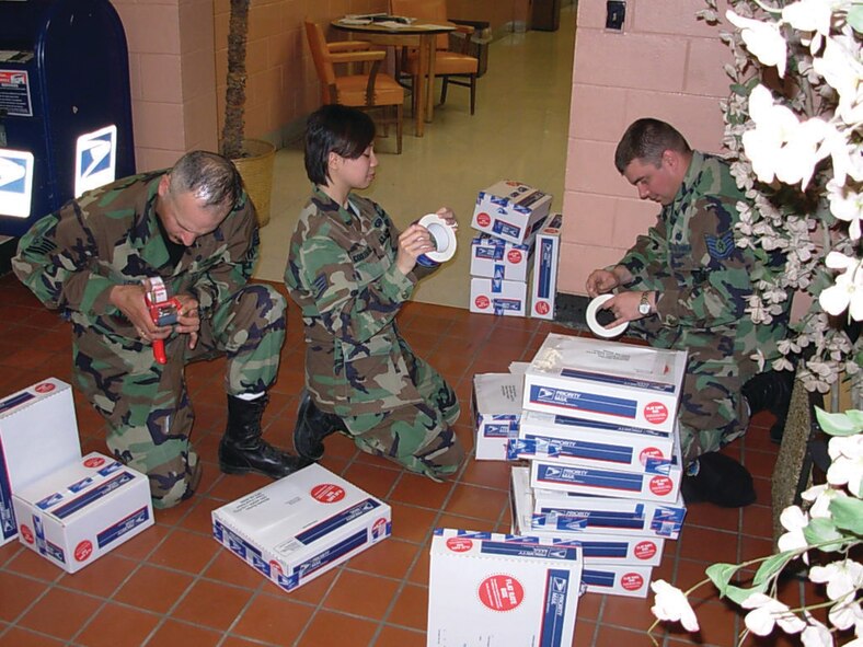 From left: Tech. Sgt. Thomas Vera, Staff Sgt. Millicent Costiniano, and Tech. Sgt. Jason Rootes,  from the 5th Communications Squadron, package supplies of pens, pencils, notebooks and more to send to Master Sgt. Michelle Rootes, 5th Medical Operations Squadron and Jason’s wife, who is deployed to Afghanistan and volunteering to help a local school. (courtesy photo)
