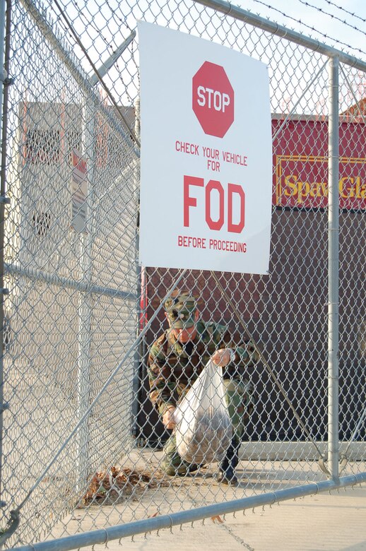 Lt. Col. Charles Combs, 433rd Aircraft Maintenance Squadron commander, clears debri from the bottom of a gate leading onto the flight line during the May wing wide Foreign Object Damage Prevention walk. Members from every work center wandered parking lots, flight line areas and roadways picking up anything that could cause damage to tires, aircraft engines or harm personel. (U.S. Air Force Photo by Tech. Sgt. Collen McGee)