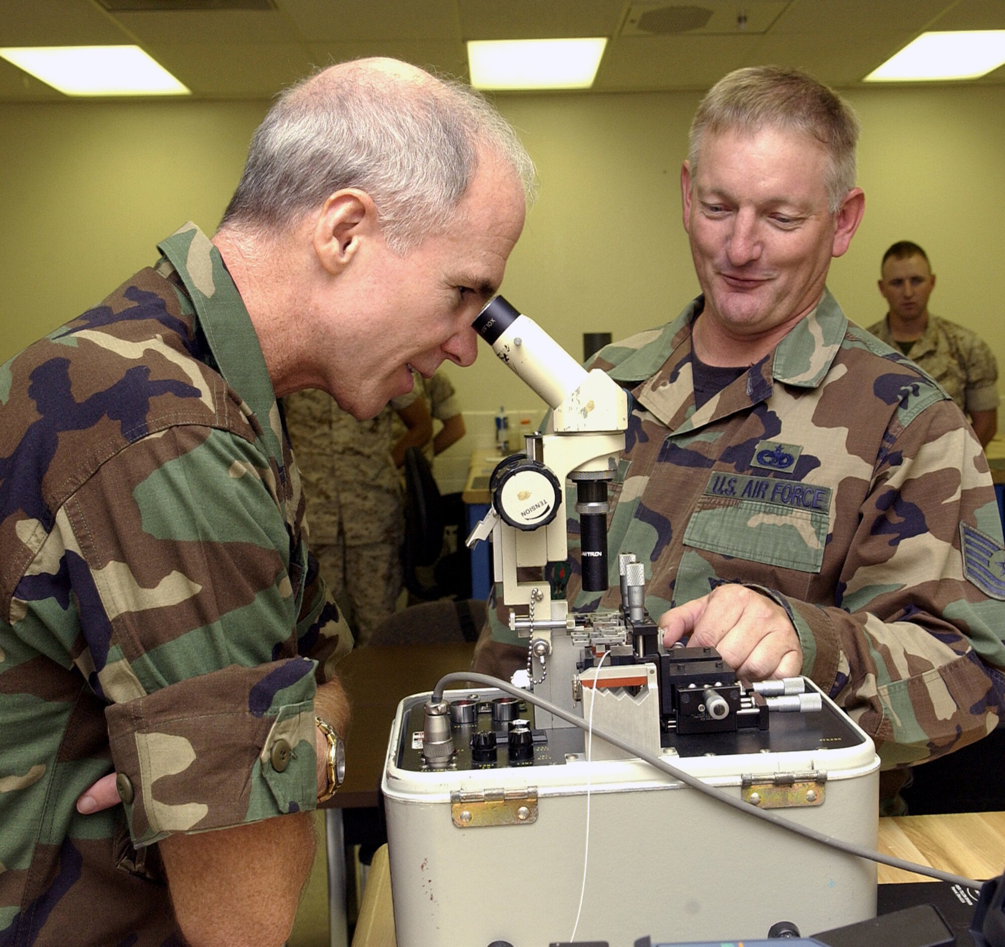 Brig. Gen. Richard Devereaux, 82nd Training Wing commander, looks into a fiber optic fusion splicer as Tech. Sgt. Steven Baker, an instructor at the 364th Training Squadron, explains how the machine works. (U.S. Air Force photo/Mike Litteken)