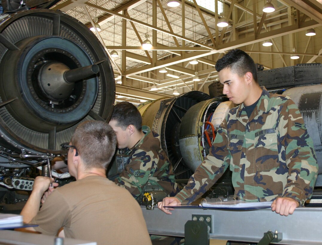 Airman 1st Class Matthew Vela, right, keeps an eye on a technical order and classmates as they work on an aircraft engine. Airman Vela graduated from the 361st Training Squadron Sept. 15. His father, Master Sgt. Jon Vela, was serving as the training manager for the 365th TRS while his son was in technical school here. (U.S. Air Force photo/Robert Fox)