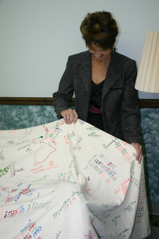 Sharon Wilkerson, an employee at the civilian personnel flight, holds a table cloth that bears the names of people who have worked in the flight. The cloth has been signed by members of the office during Christmas since 1948. (U.S. Air Force photo/Robert Fox)