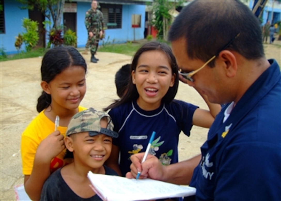 U.S. Navy Petty Officer 1st Class Allen Borromeo Yabut (right) signs his name and enters his e-mail address in the notebooks of Pasobolong Elementary School students in Zamboanga, Philippines, on Oct. 26, 2006.  Sailors from the amphibious dock landing ship USS Harpers Ferry (LSD 49) visited the school with Joint Special Operations Task Force-Philippines as part of a service project to aid impoverished areas in the communities of the Philippines.   