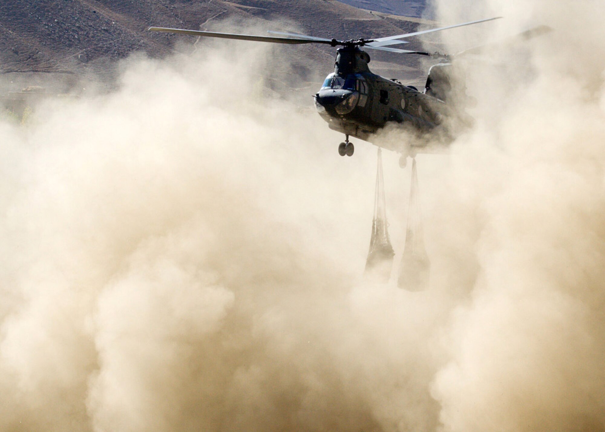 Humanitarian assistance is dropped into the Panjshir Province's Paryan District Oct. 28. At nearly 10,000 feet above sea level, Paryan has the highest elevation of the six districts in the Panjshir Valley. Since the rough and narrow road to the district cannot support truck transport, helicopter airlift of supplies was necessary. Using slings around pallets of food supplies, a Chinook helicopter's crew prepares to drop off one of two loads totaling four tons to help the district's 38,000 residents prepare for winter. (U.S. Air Force photo/Tech. Sgt. John Cumper)