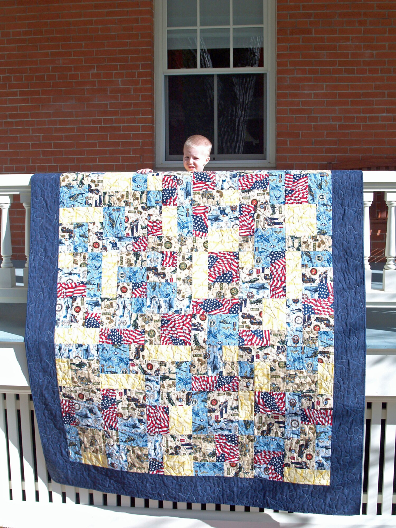 Zachary Angerman, son of Maj. Scott Angerman and Mrs. Tana Angerman, holds his mother's finished quilt in front of their home.  Quilts of Valor also encourages child participation in making the quilts for wounded servicemembers.